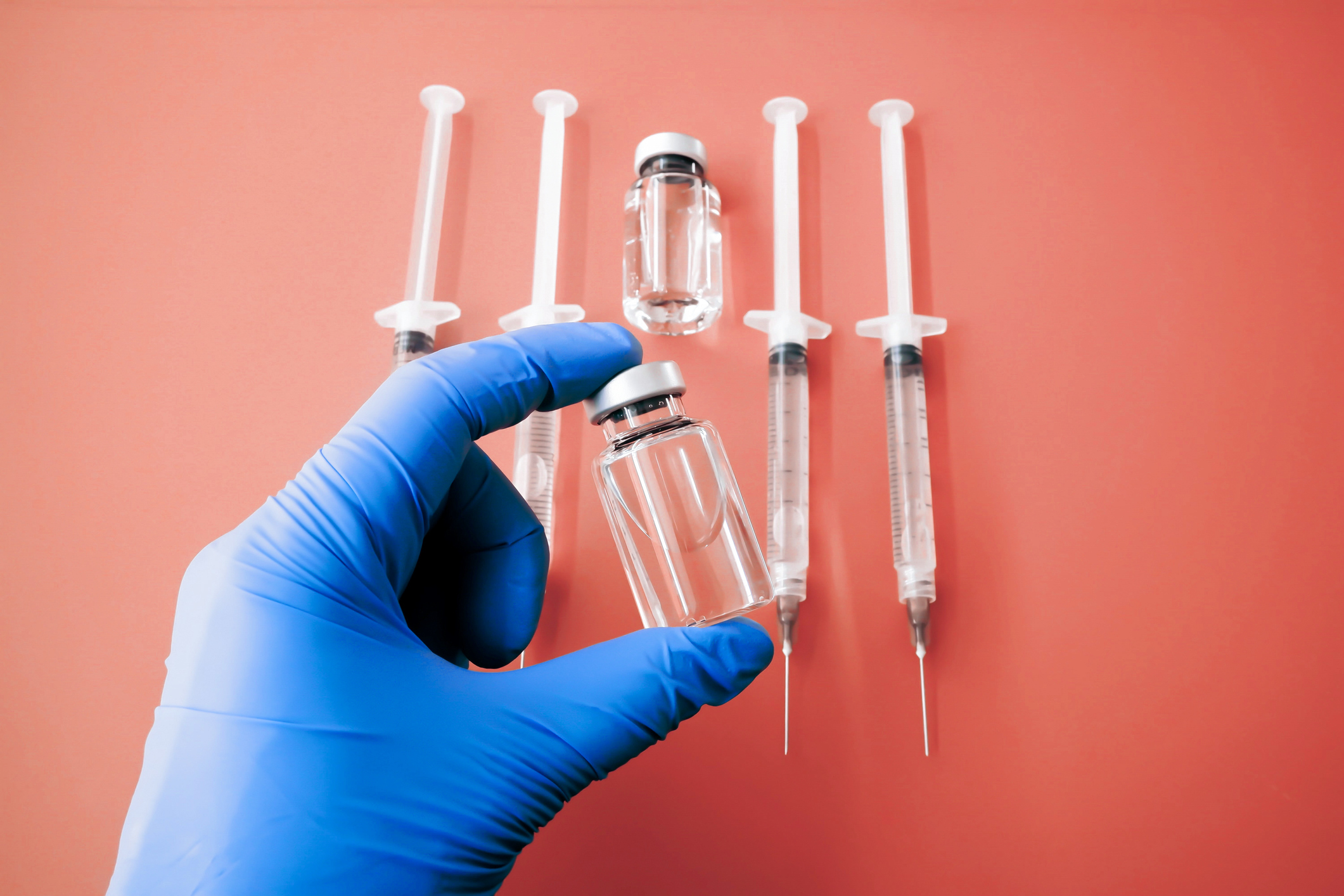 Gloved Hand Holds Medical Vial Above Orange Background