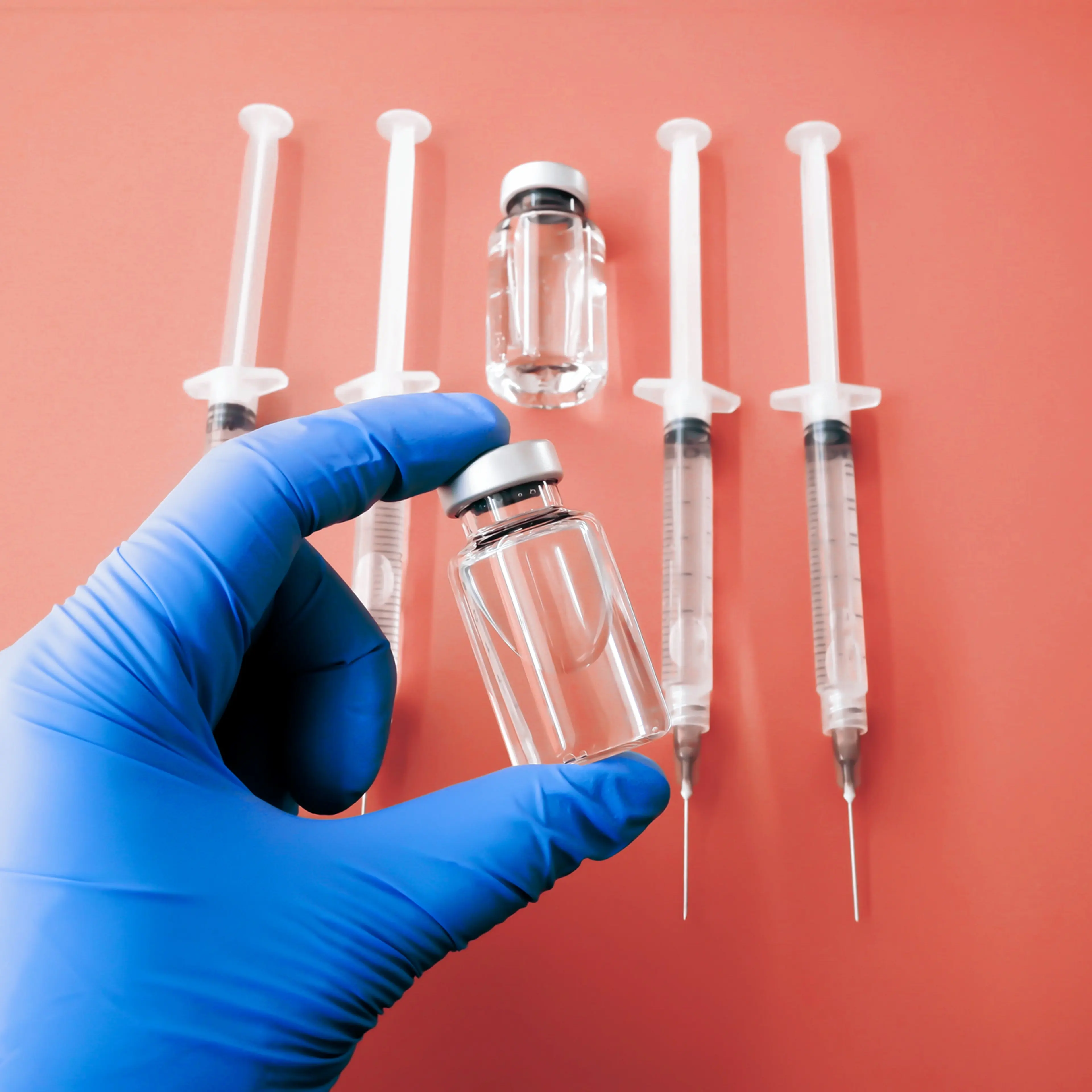Gloved Hand Holds Medical Vial Above Orange Background