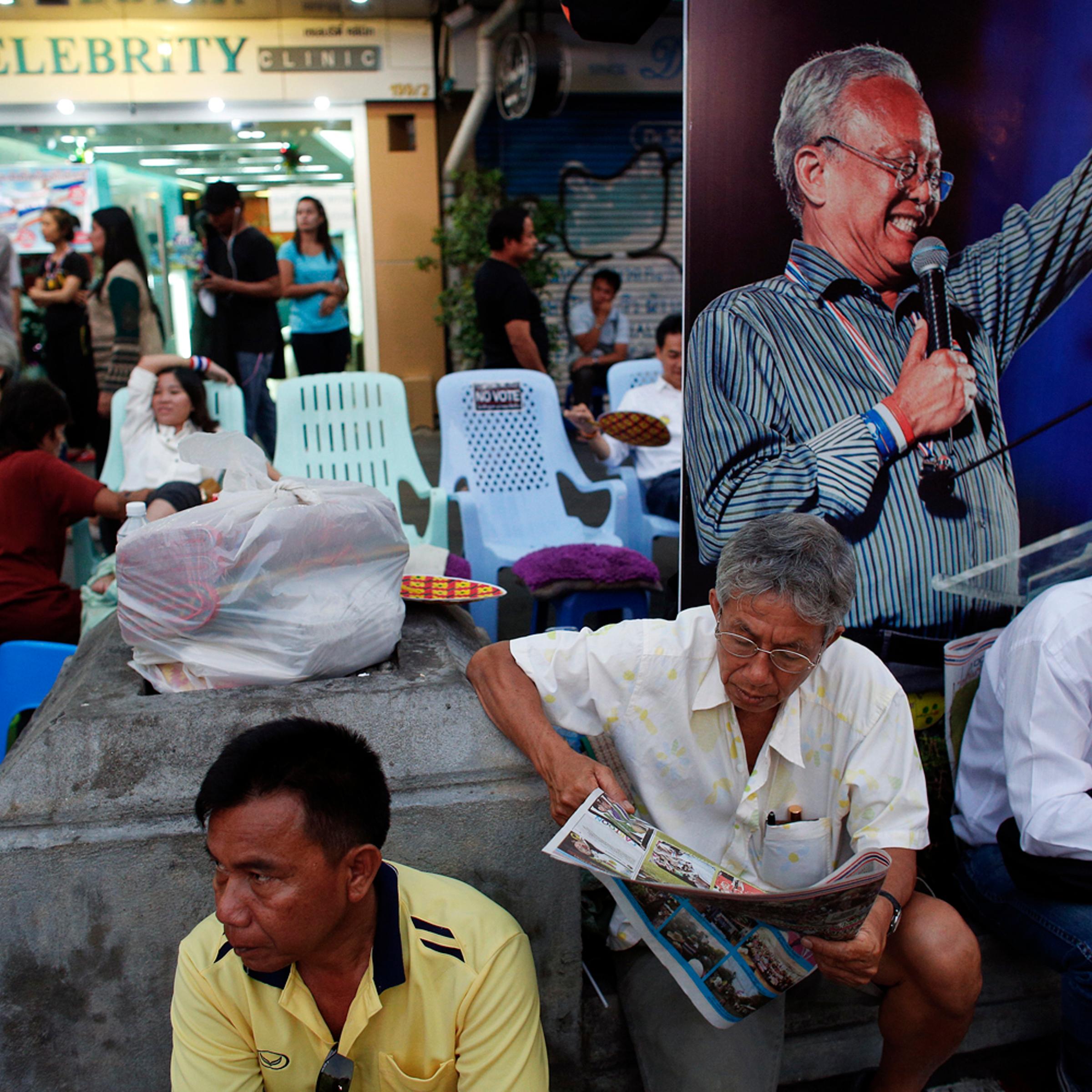 Anti-government protesters enjoy a massage and read papers near a picture of protest leader Suthep Thaugsuban in an occupied area, in downtown Bangkok