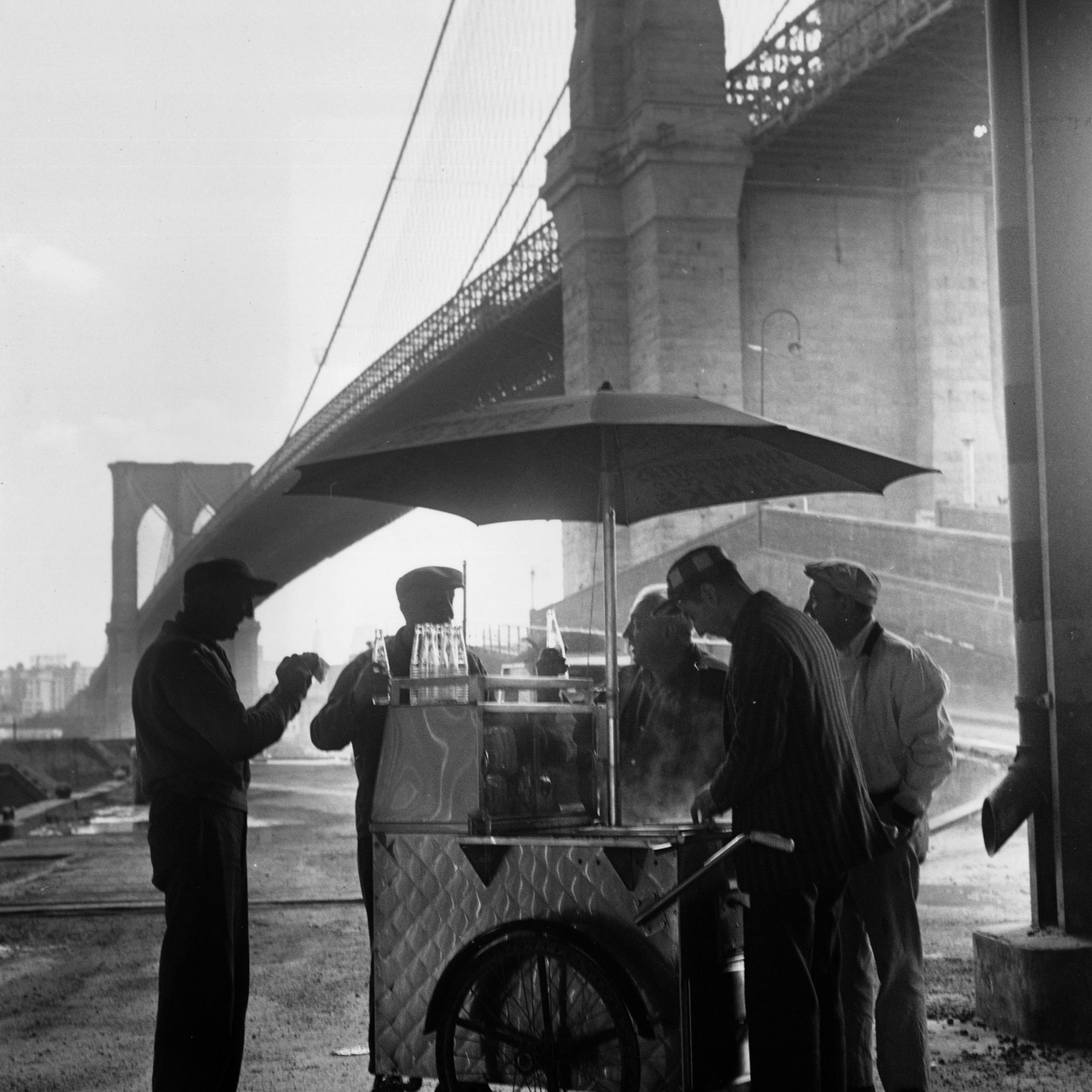 A group of workers getting refreshments from a portable snack stand underneath Brooklyn Bridge.