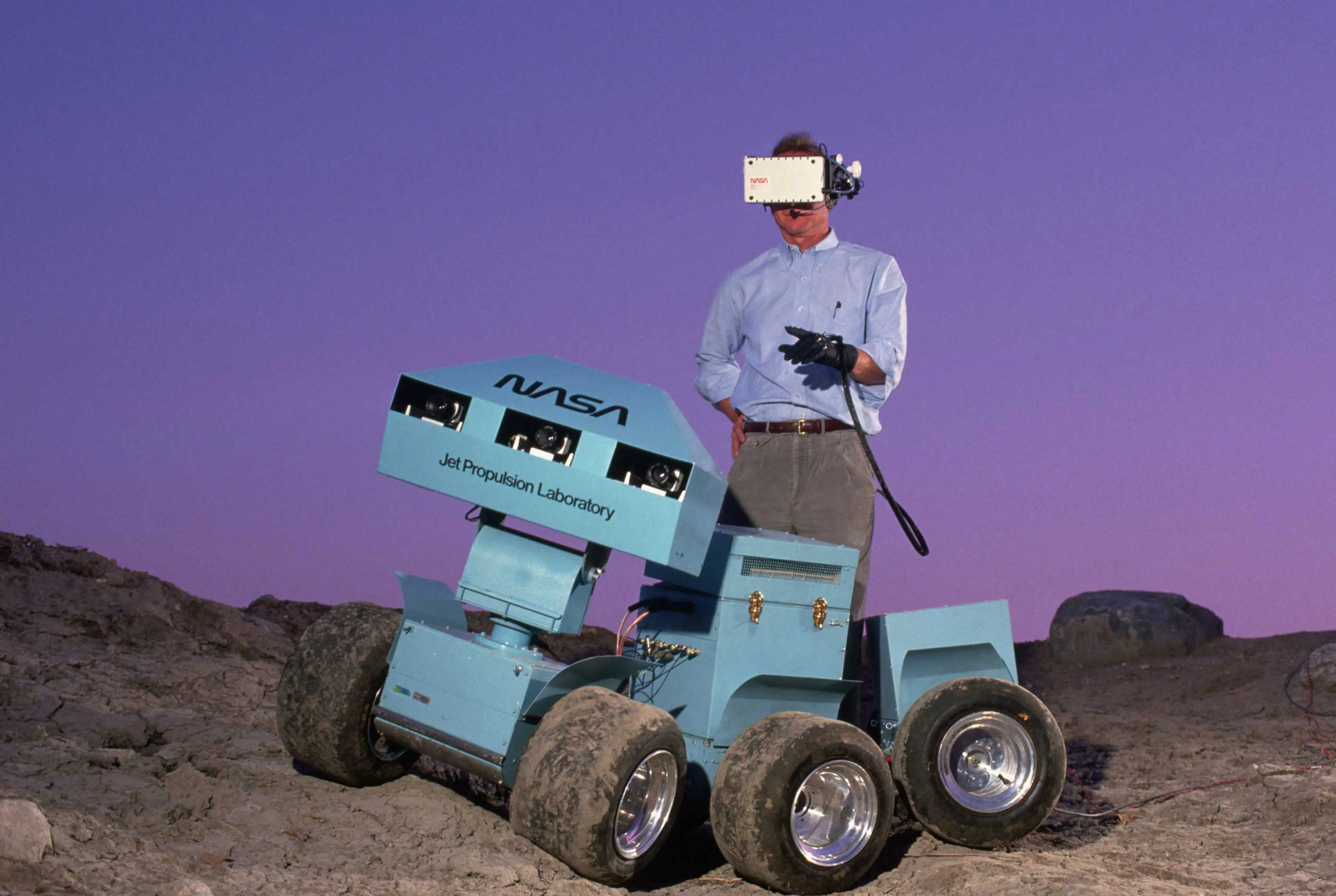 Andrew Mishkin wearing a 3-D virtual display helmet that is connected to a six-wheeled roving vehicle. The rover was meant to explore the surface of Mars and send back information.