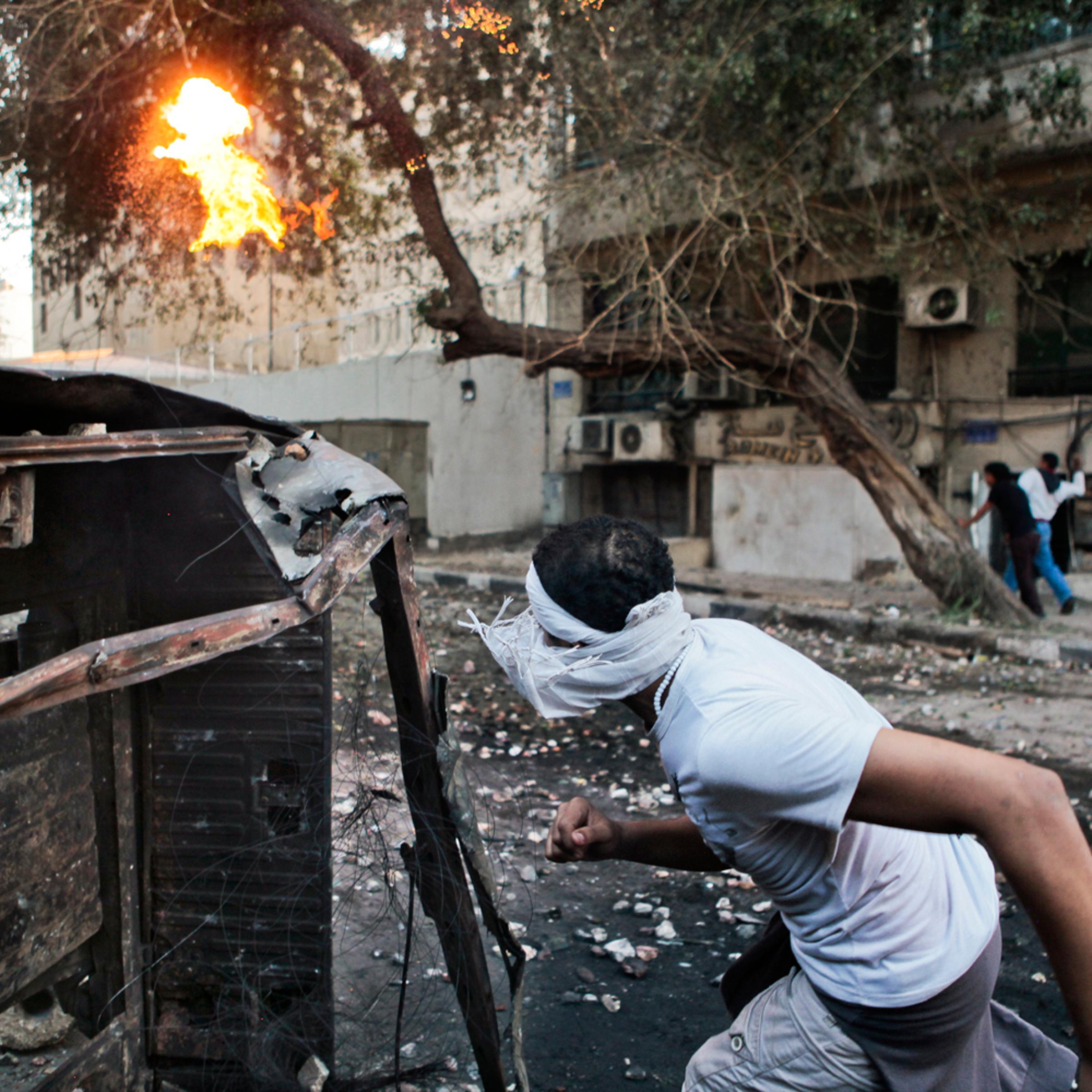 Nov. 28, 2012. An Egyptian protester finds cover behind a destroyed vehicle at the scene of clashes with police near Tahrir Square in Cairo. In conjunction with <a href="http://world.time.com/2012/11/28/morsis-moment/">"Morsi's Moment."</a>