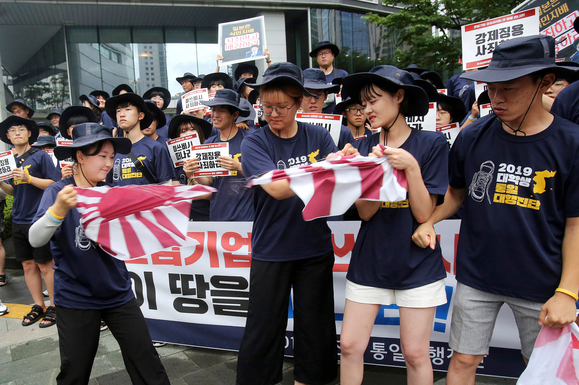 South Korean college students tear a banner showing an image of a Japanese rising sun flag during a rally to denounce Japan's new trade restrictions on South Korea in front of the office of Mitsubishi Corp. in Seoul, South Korea, on Aug. 7.