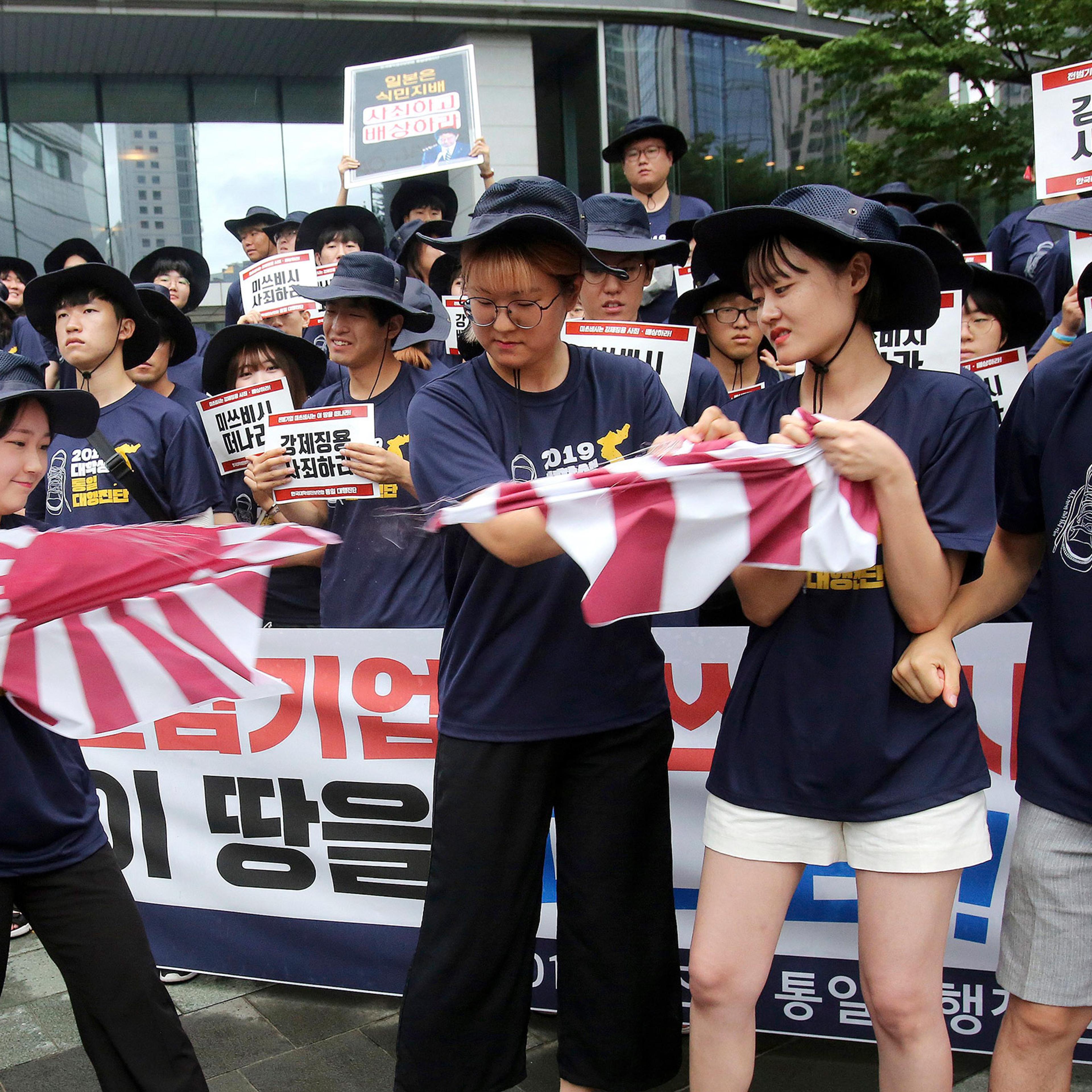 South Korean college students tear a banner showing an image of a Japanese rising sun flag during a rally to denounce Japan's new trade restrictions on South Korea in front of the office of Mitsubishi Corp. in Seoul, South Korea, on Aug. 7.