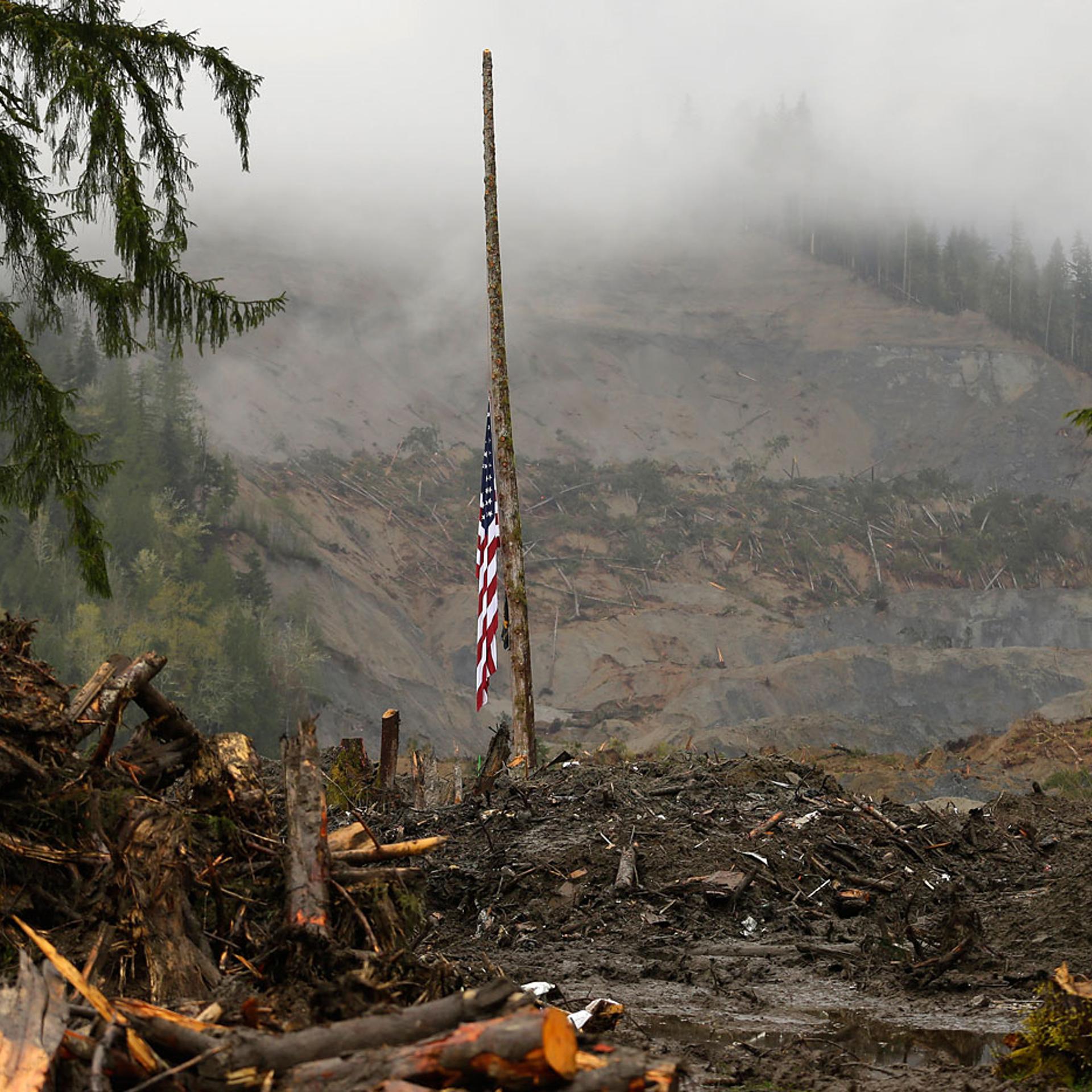 A flag rests at half staff on a cedar pole, Wednesday, April 16, 2014, with the face of the massive deadly mudslide that hit the community of Oso, Wash. on March 22, 2014 behind it.