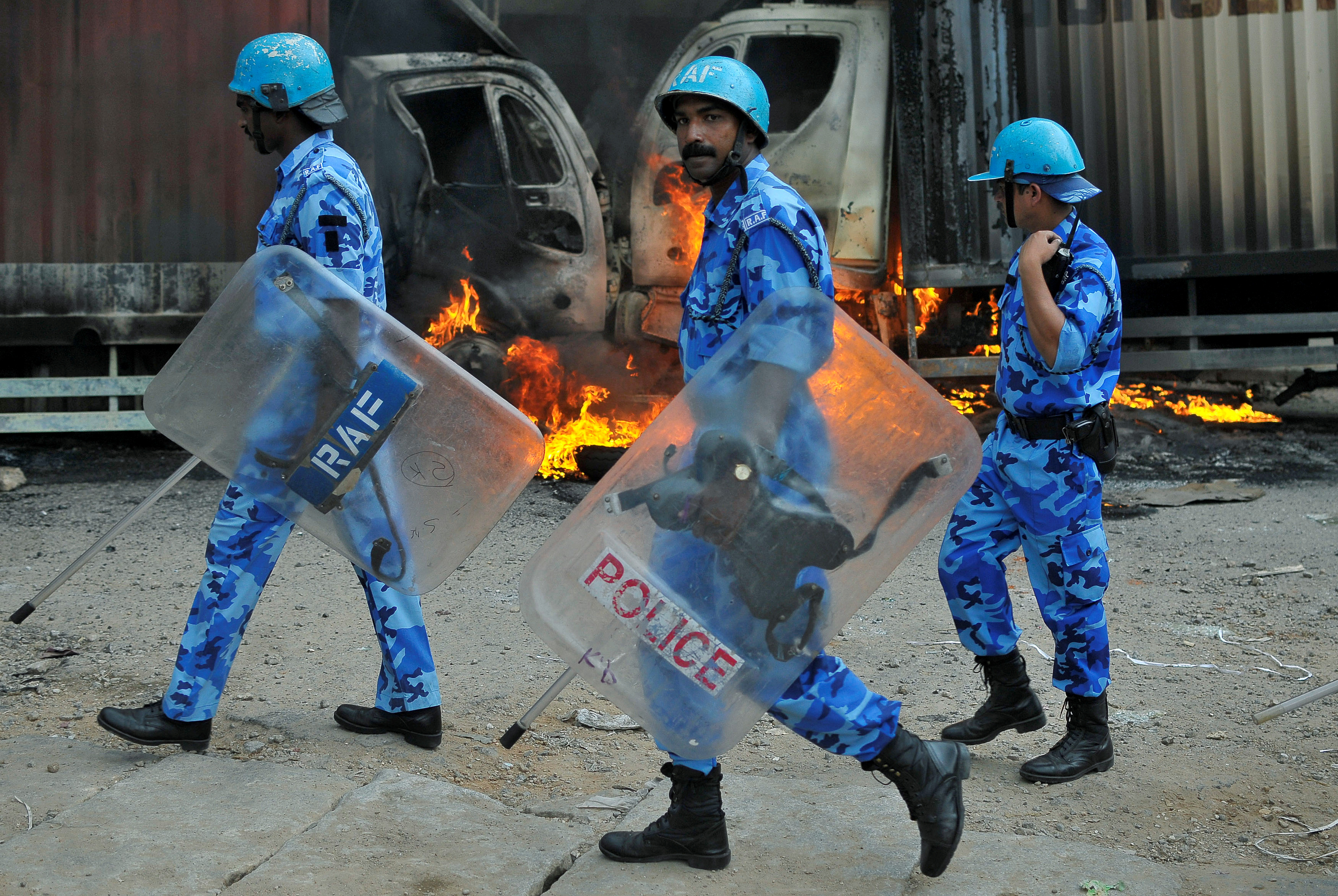 Members of the security forces make their way past burning lorries in Bengaluru