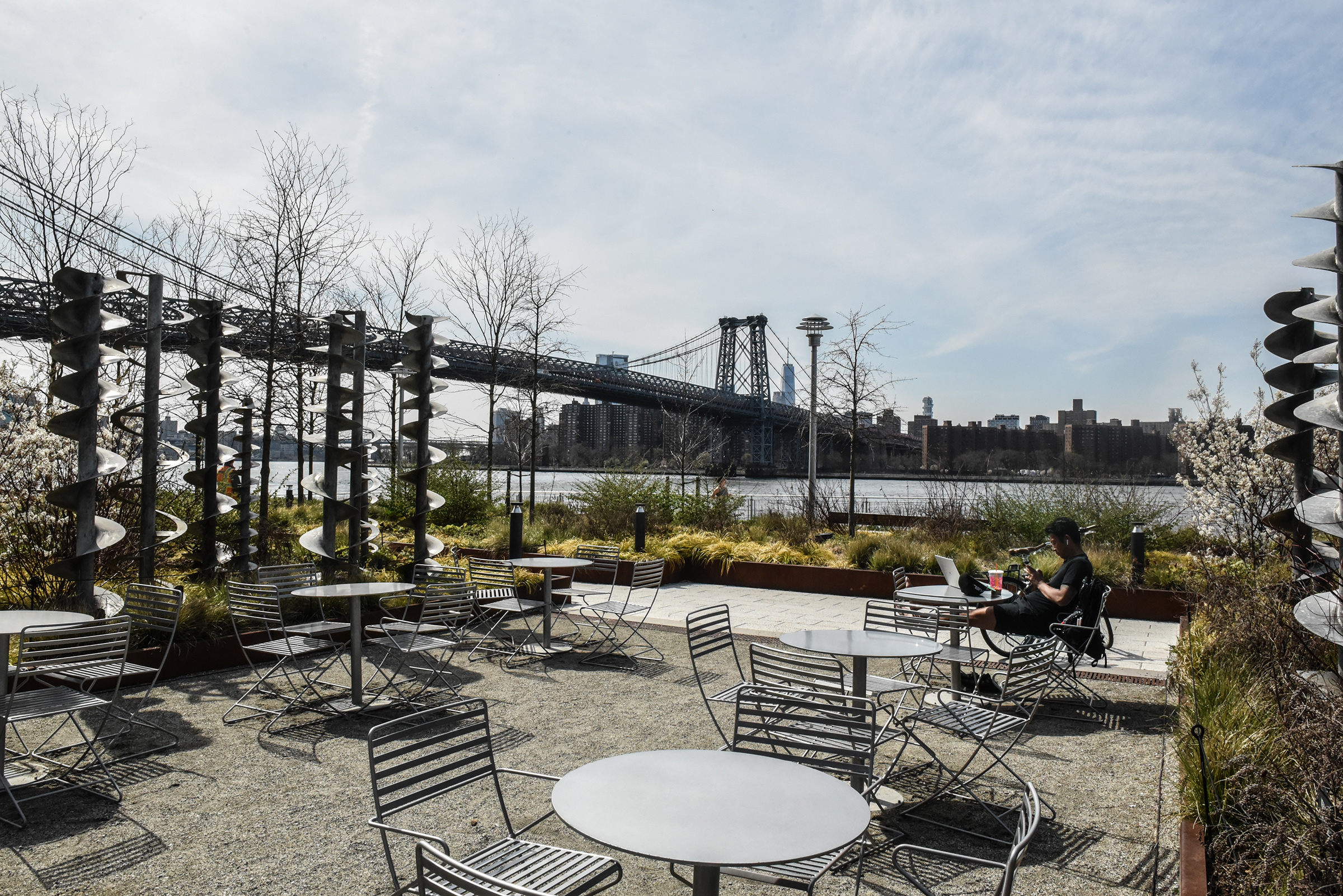 A person sits amongst empty tables and chairs at Domino Park in Williamsburg, Brooklyn on April 7
