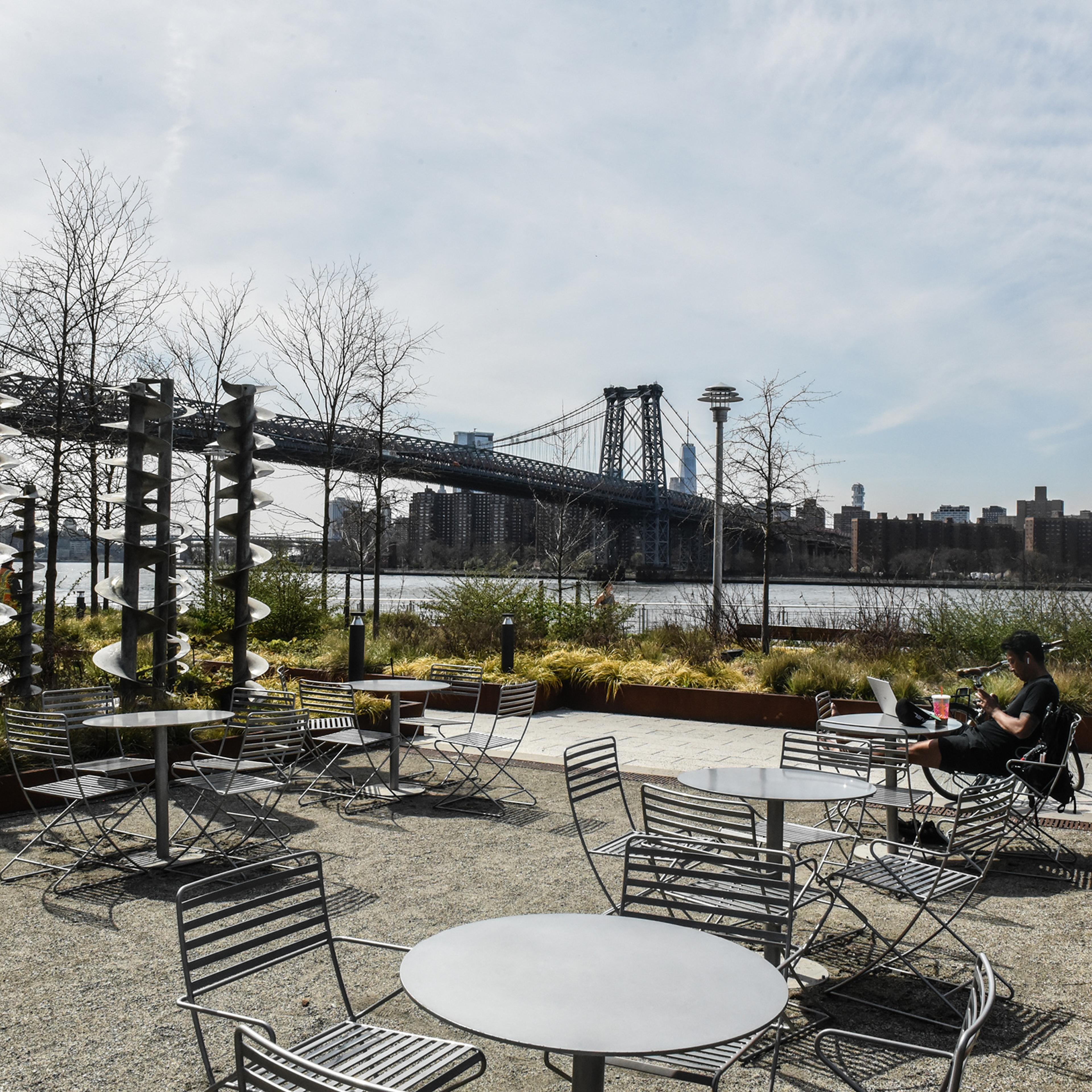 A person sits amongst empty tables and chairs at Domino Park in Williamsburg, Brooklyn on April 7