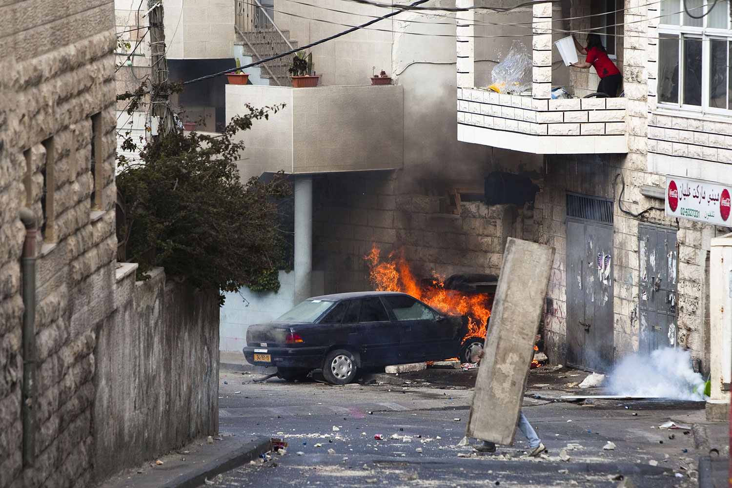 A Palestinian youth takes cover as a woman tries to put out a fire in a burning car in the East Jerusalem neighborhood of Issawiya, Israel, on May 13, 2011. 