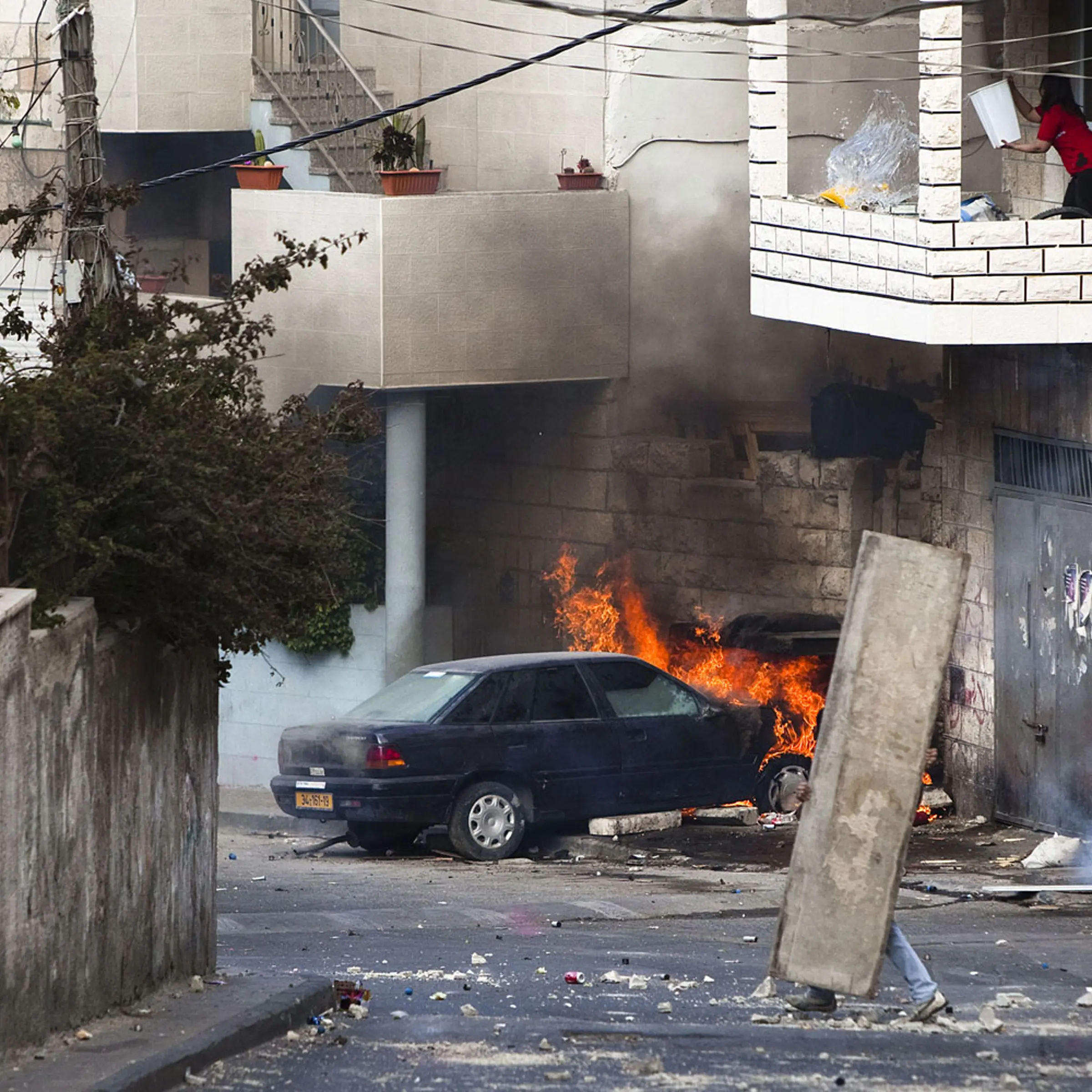 A Palestinian youth takes cover as a woman tries to put out a fire in a burning car in the East Jerusalem neighborhood of Issawiya, Israel, on May 13, 2011.