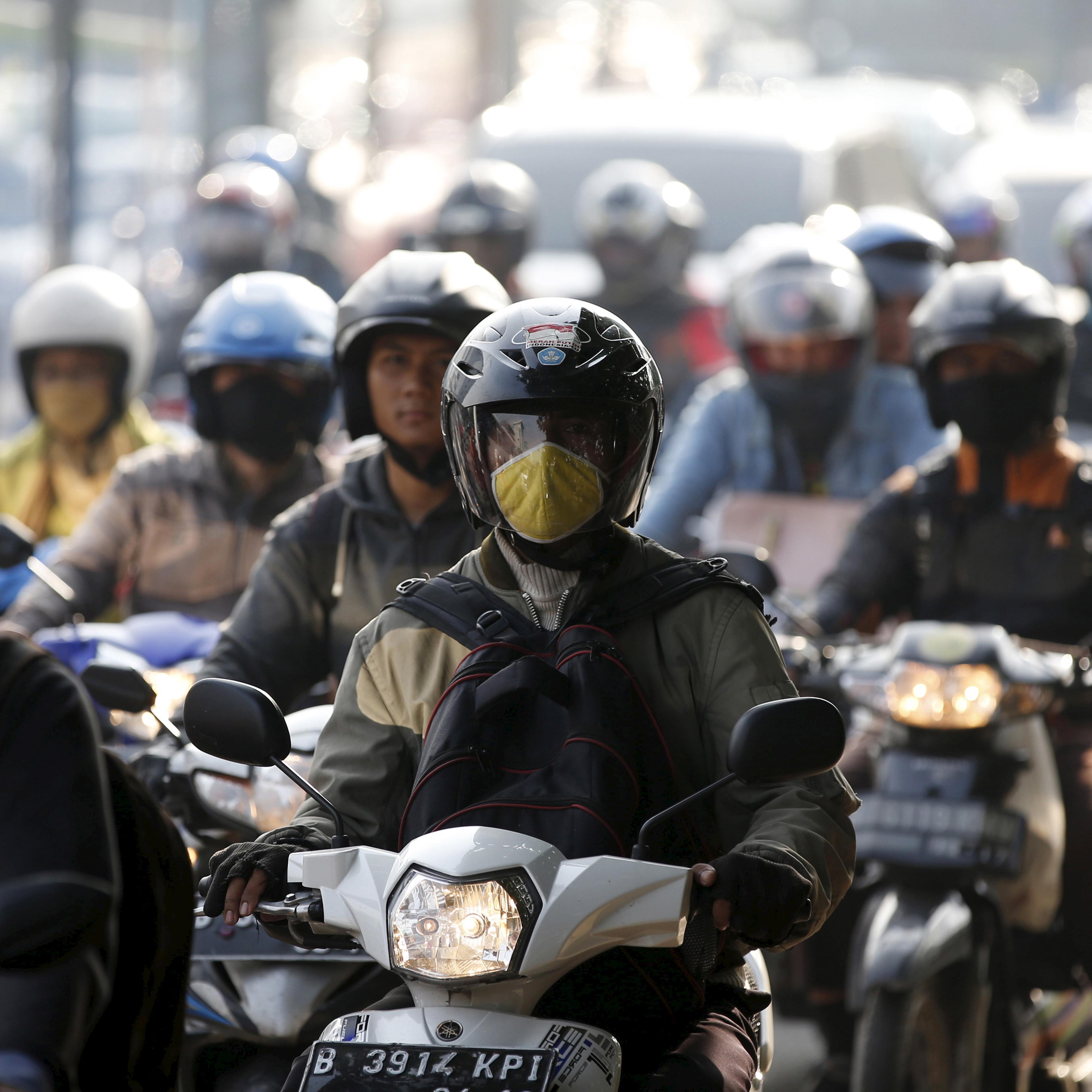 Motorcyclists ride on a major route next to a toll road into Jakarta