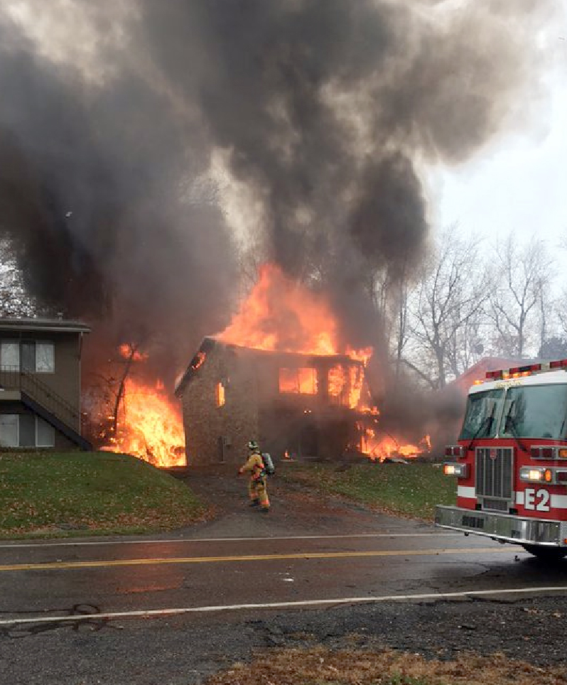 A firefighter walks up a driveway as an apartment building burns, where a small business jet crashed in Akron, Ohio on Nov. 10, 2015.