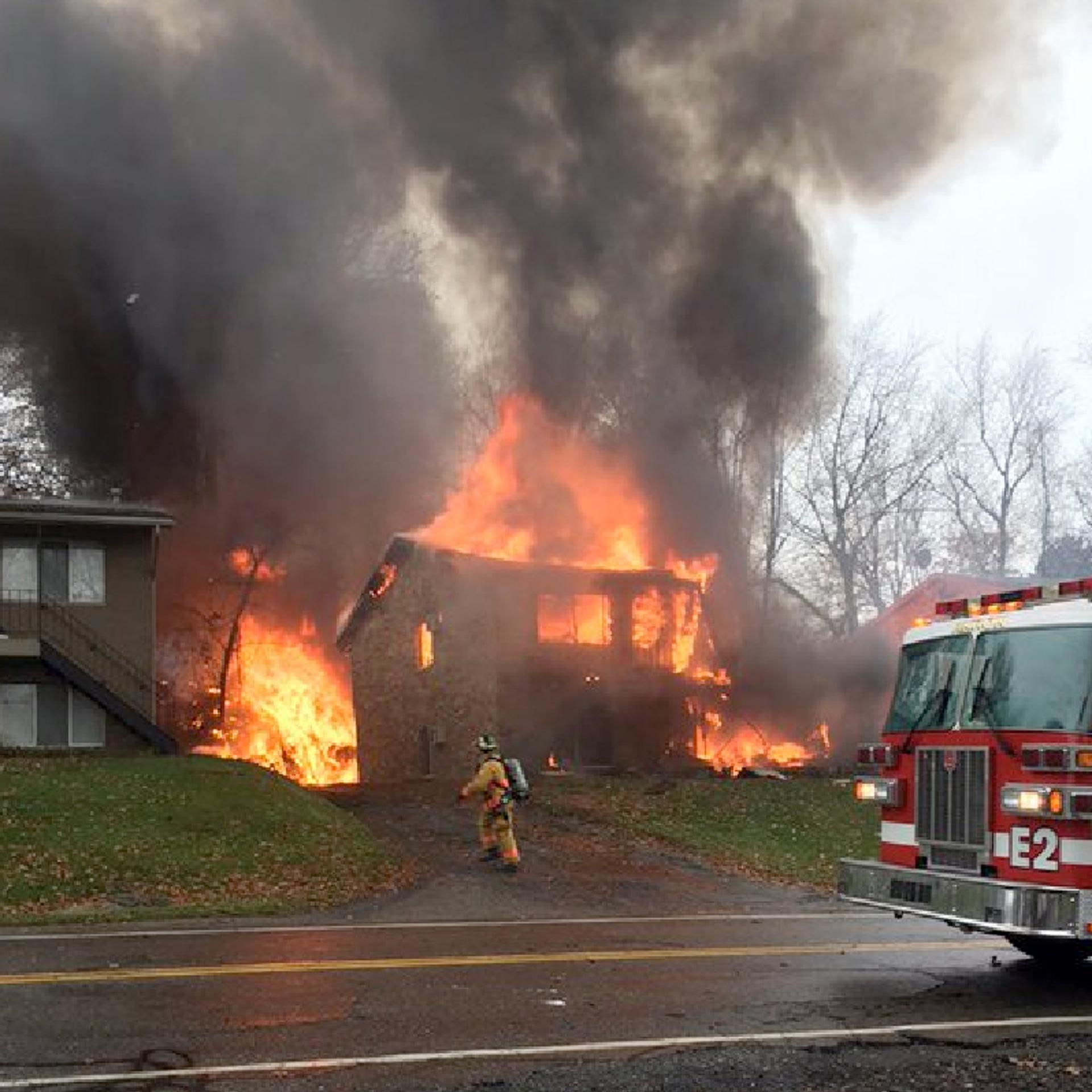 A firefighter walks up a driveway as an apartment building burns, where a small business jet crashed in Akron, Ohio on Nov. 10, 2015.