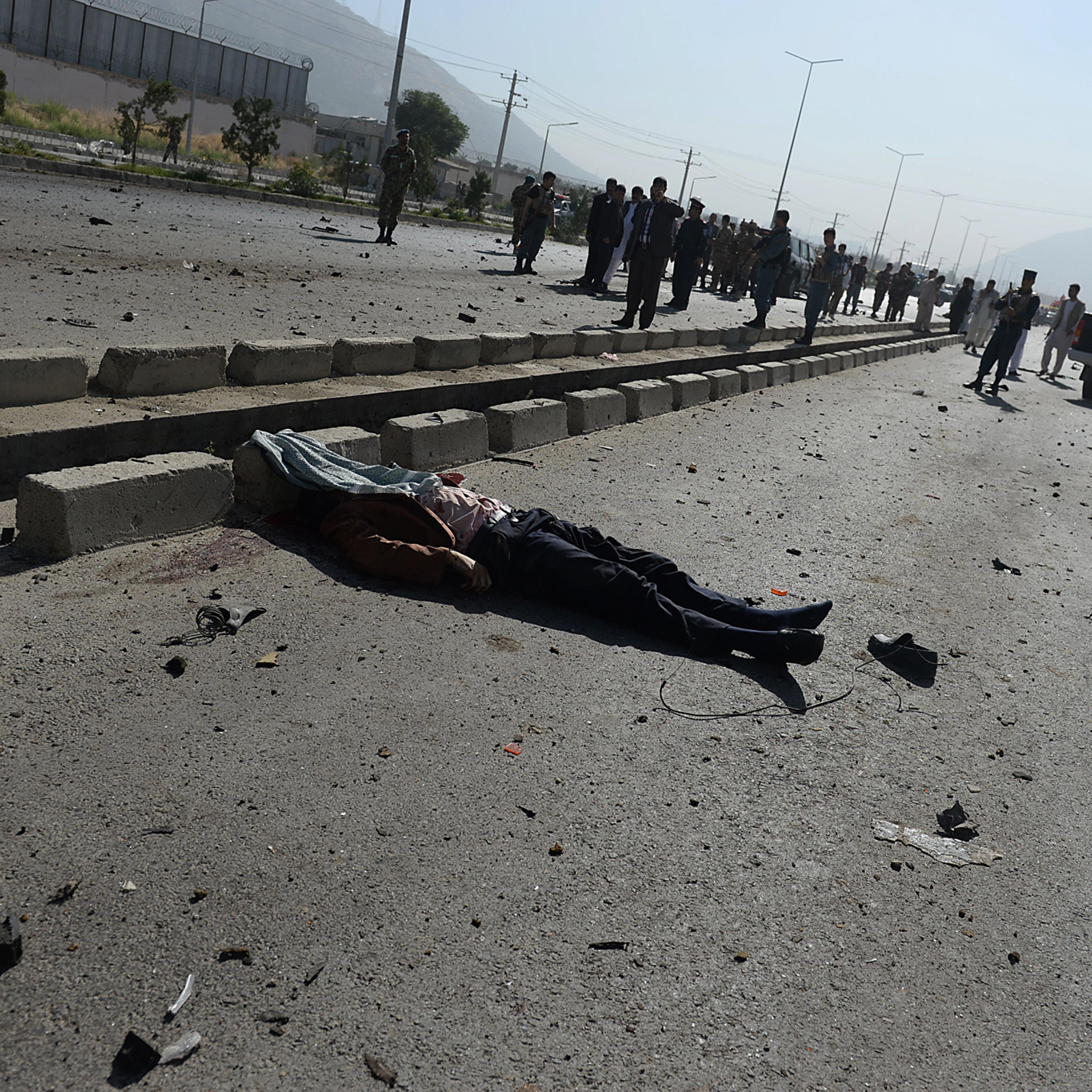 A victim's body lies on the road as Afghan security forces inspect the site of a suicide attack in Kabul on June 21, 2014.
