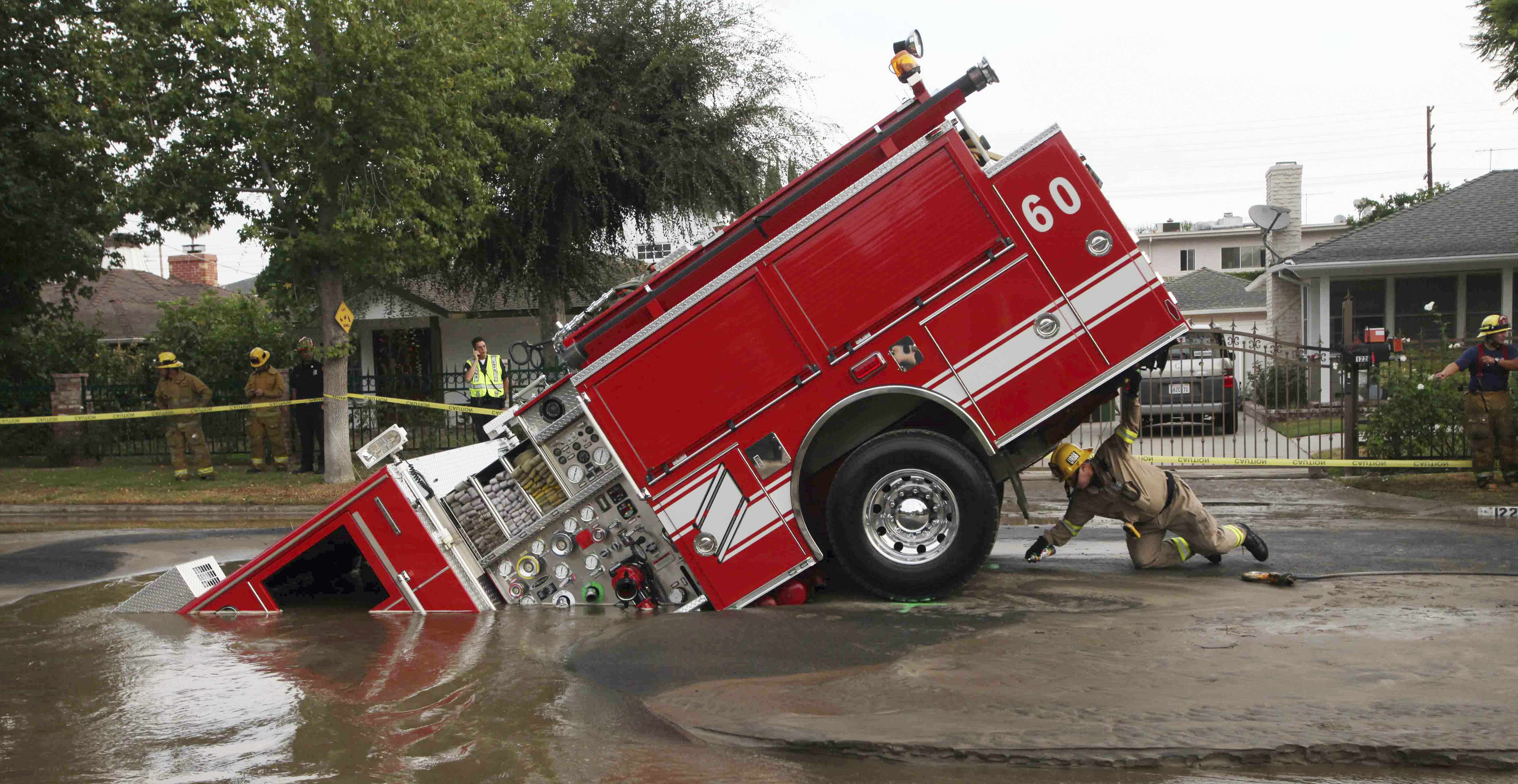 A Los Angeles fireman looks under a fire truck stuck in a sinkhole in the Valley Village neighborhood of Los Angeles, Sept. 8, 2009. Four firefighters escaped injury early Tuesday after their fire engine sunk into a large hole caused by a burst water mai