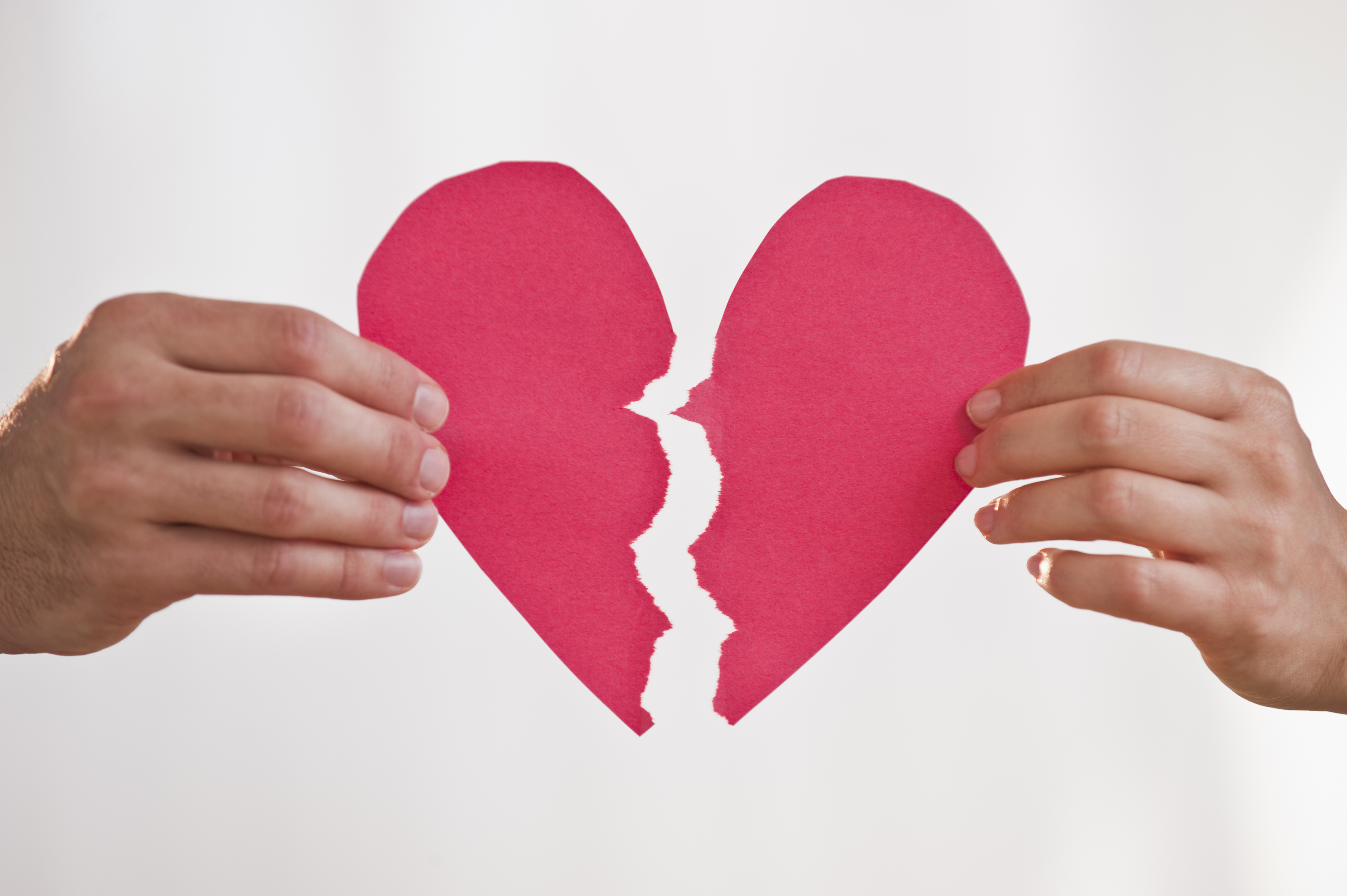 Two hands holding broken paper heart