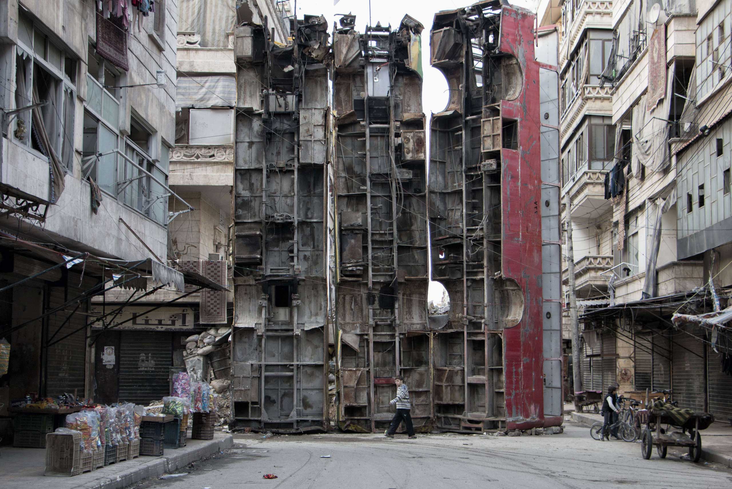 A young boy walks past a makeshift barricade made of wreckages of buses to obstruct the view of regime snipers and to keep people safe in Aleppo, Syria on March 14, 2015.