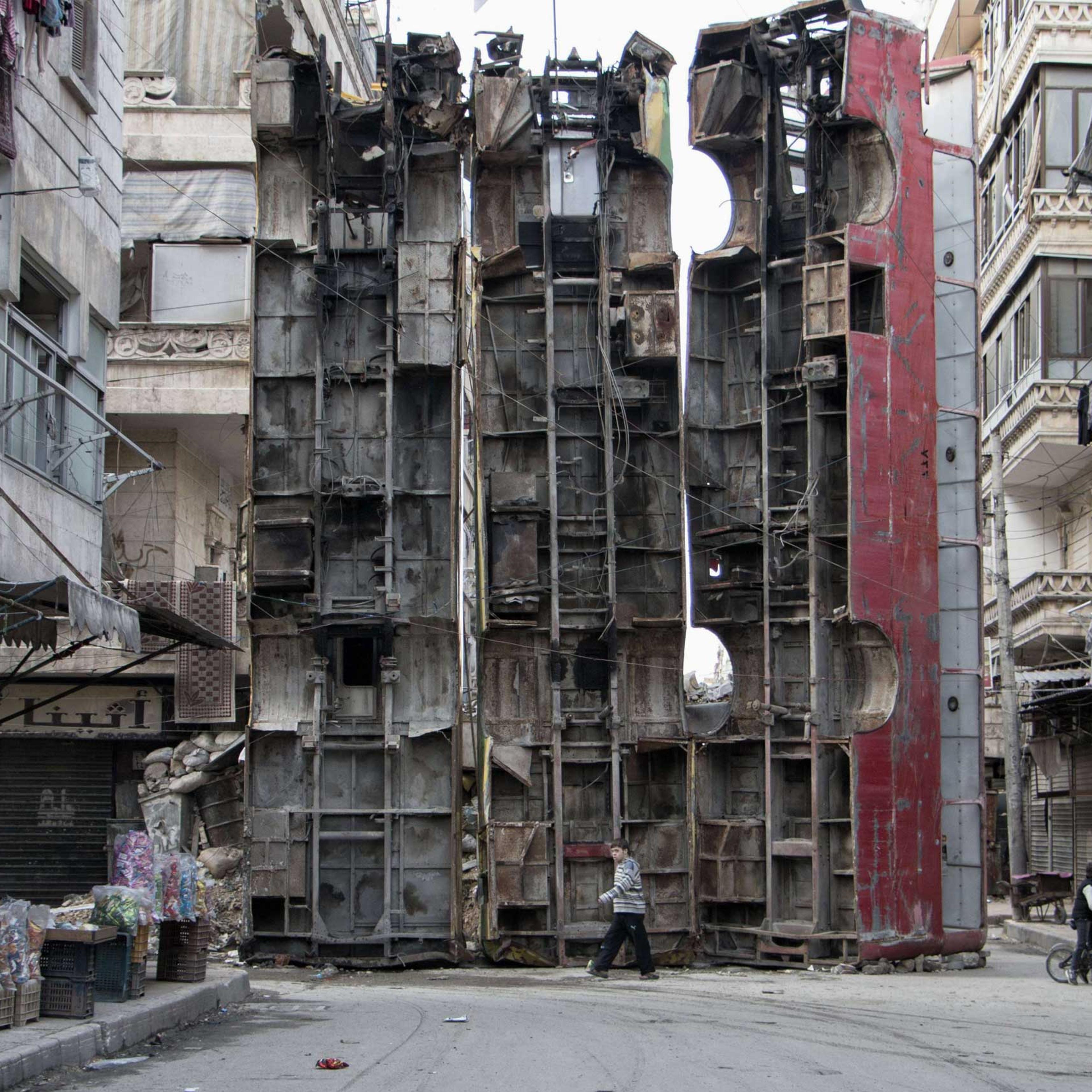 A young boy walks past a makeshift barricade made of wreckages of buses to obstruct the view of regime snipers and to keep people safe in Aleppo, Syria on March 14, 2015.