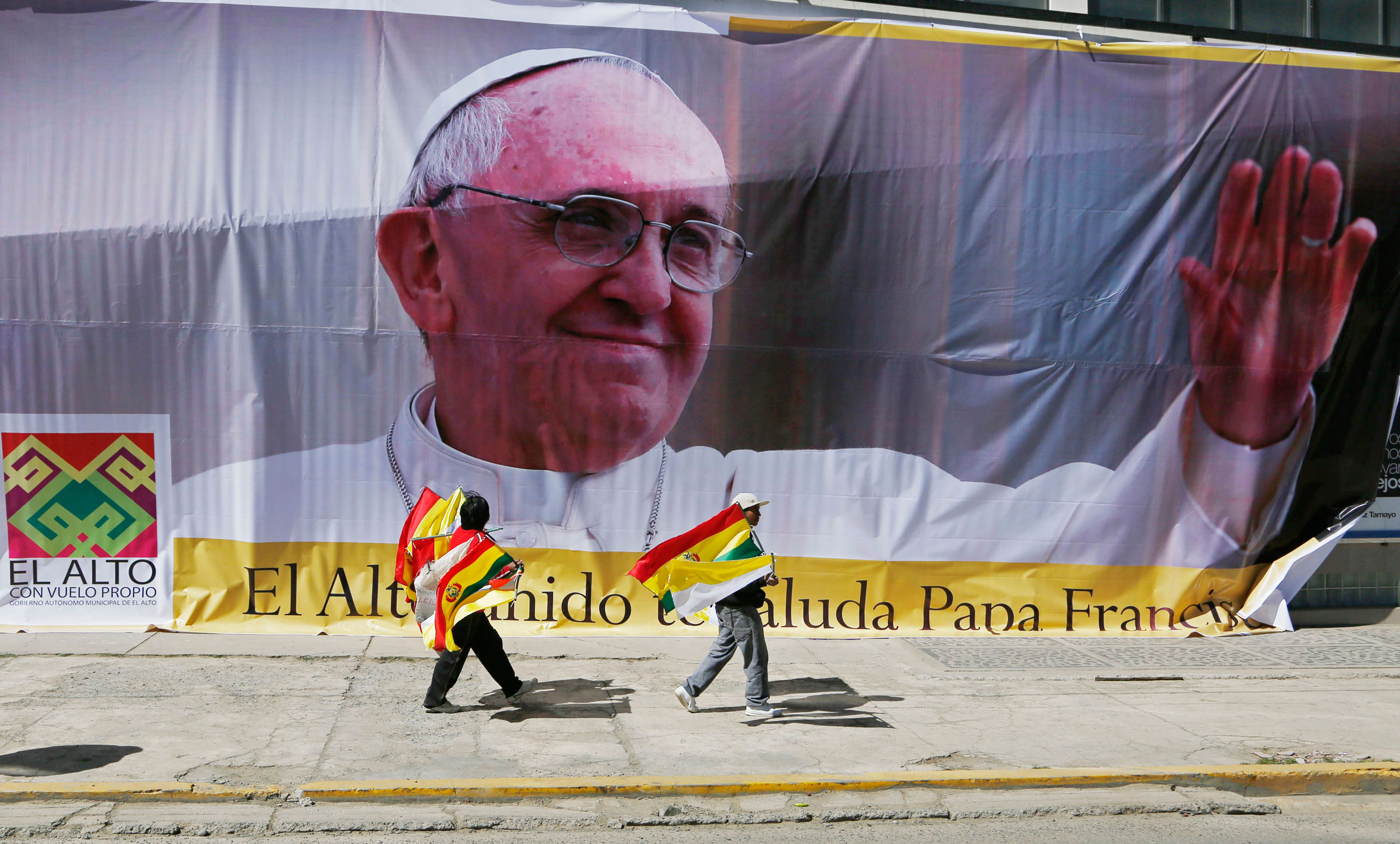 Street vendors selling Bolivian and Vatican flags pass a large image of Pope Francis ahead of the pope's arrival to El Alto, Bolivia, Wednesday, July 8, 2015. Due to the altitude, the pontiff will spend only a few hours in the capital city La Paz, which 
