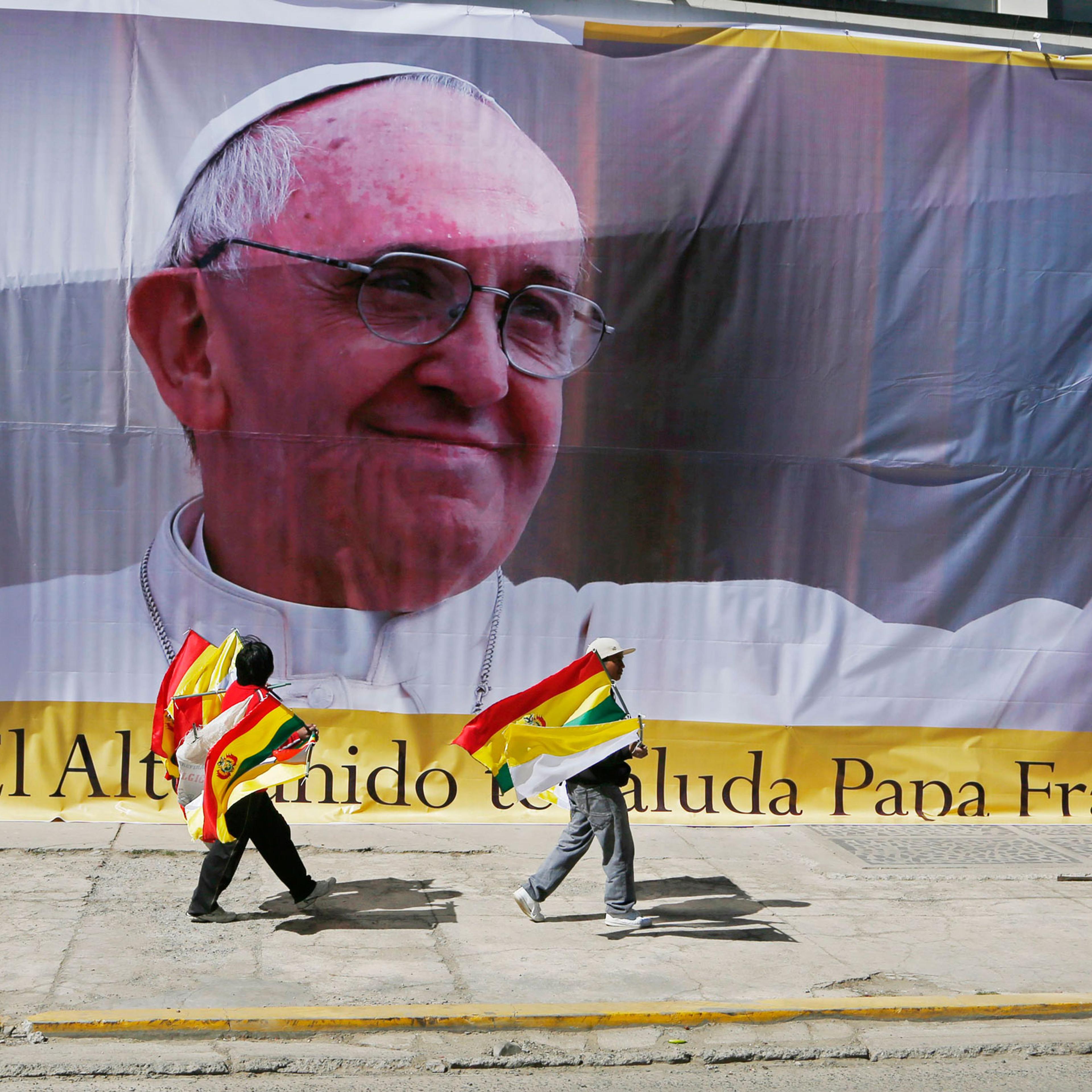 Street vendors selling Bolivian and Vatican flags pass a large image of Pope Francis ahead of the pope's arrival to El Alto, Bolivia, Wednesday, July 8, 2015. Due to the altitude, the pontiff will spend only a few hours in the capital city La Paz, which