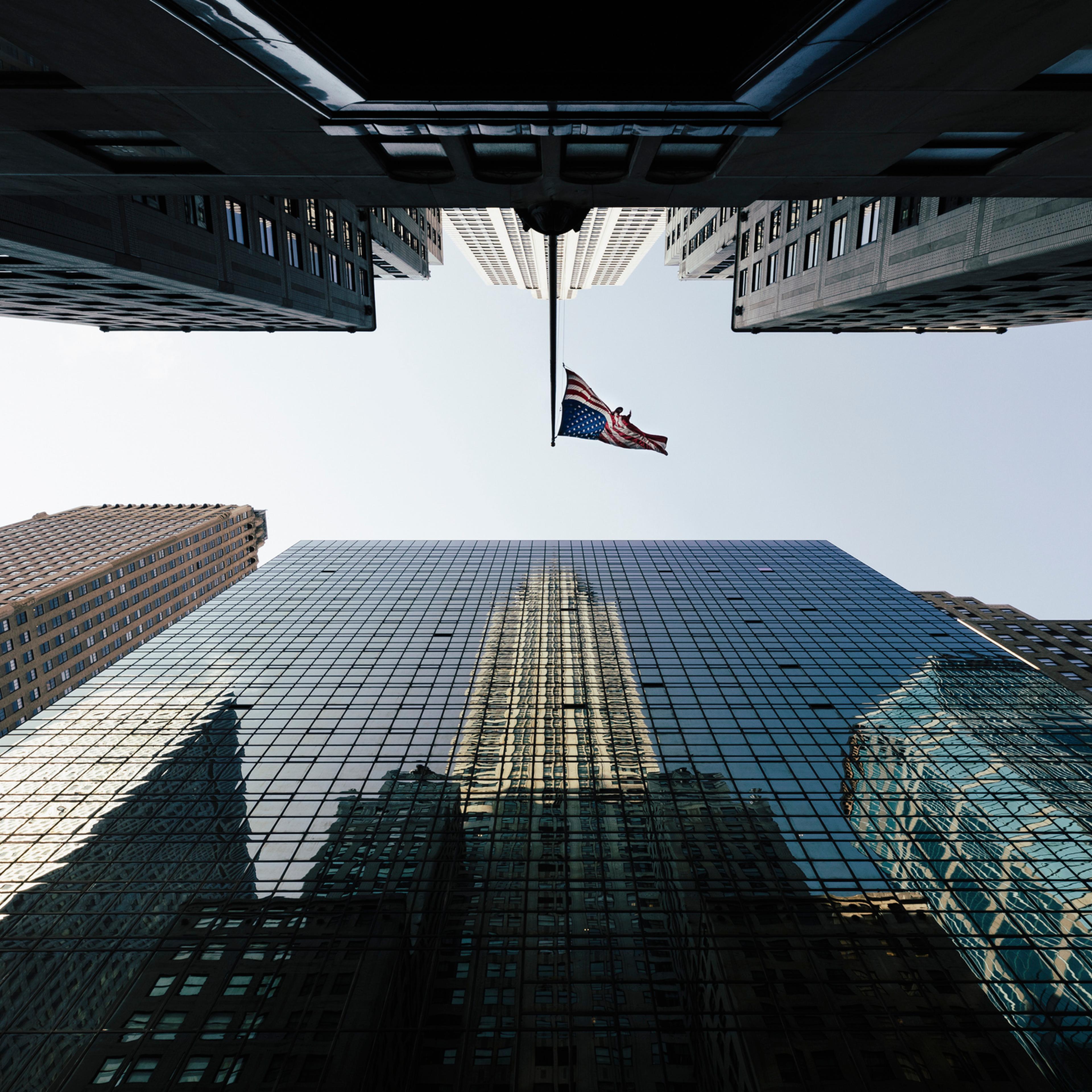 Directly below view of American Flag amidst modern office skyscrapers against sky, New York, USA