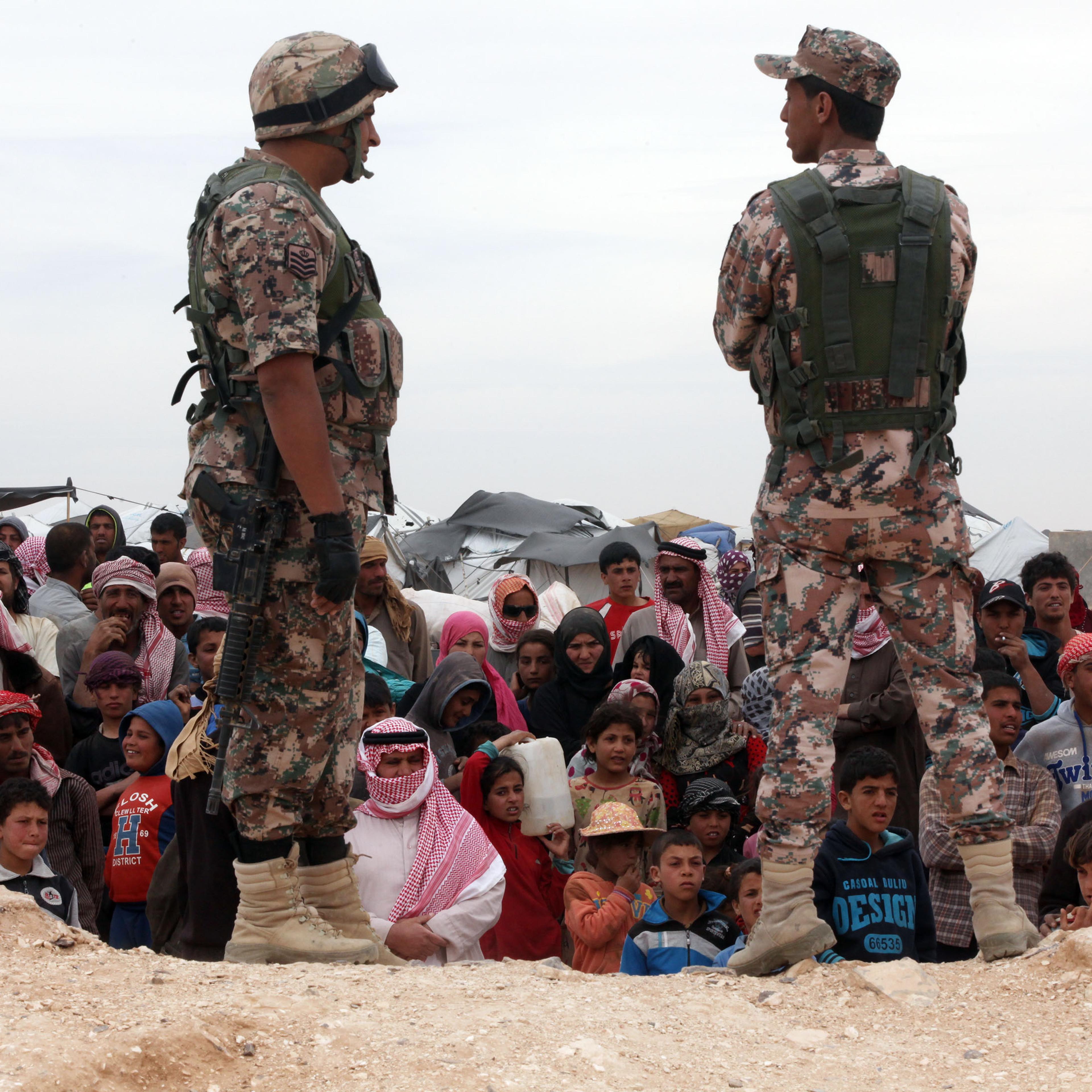 Soldiers stand near Syrian refugees who have arrived at the Jordanian military crossing point of Hadalat at the border with Syria after a long walk through the Syrian desert in Hadalat, Jordan, on May 4, 2016.