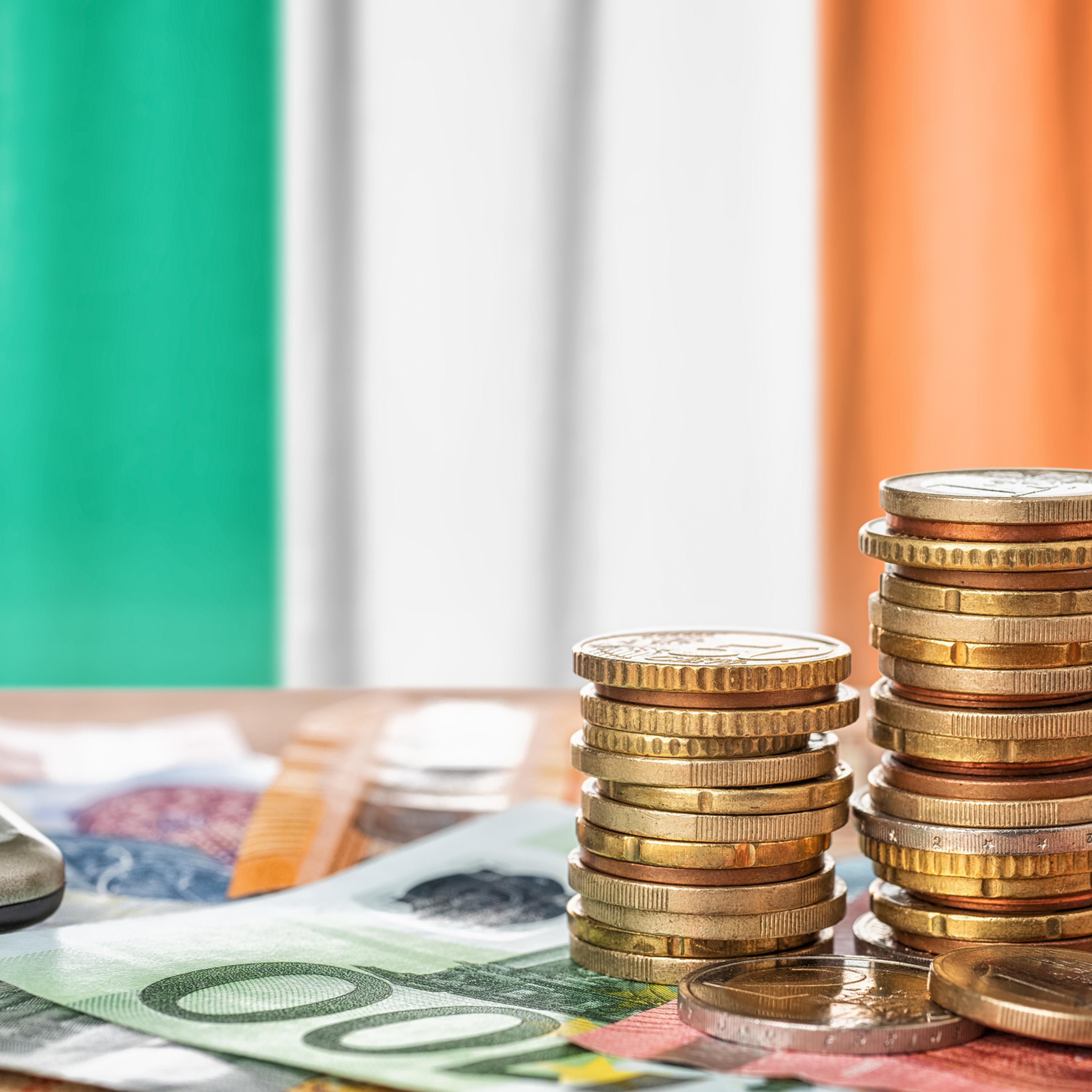 Euro banknotes and coins in front of the national flag of Ireland