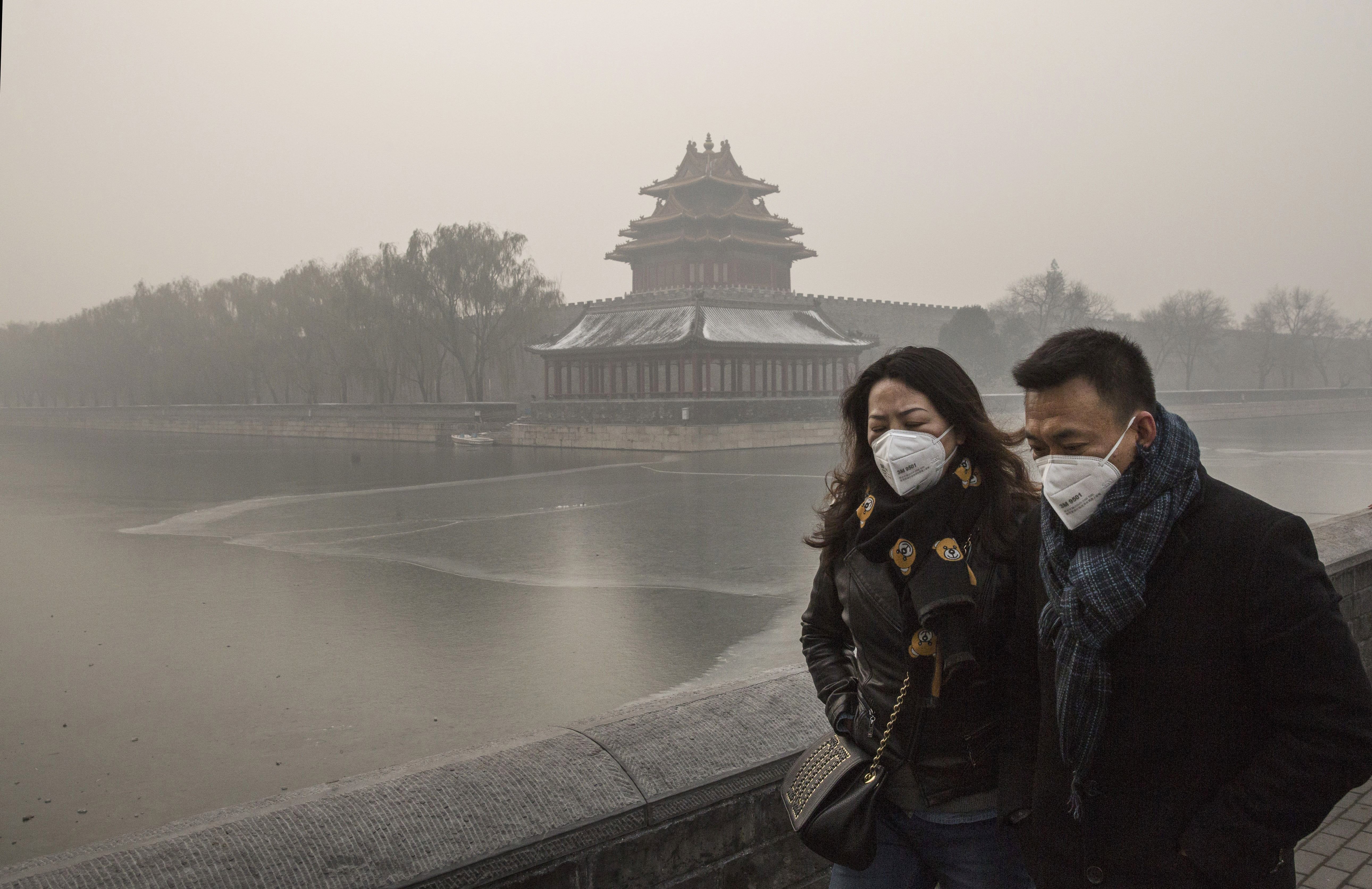 A couple wear protective masks as they walk outside the Forbidden City on a day of heavy pollution in Beijing on Nov. 30, 2015.