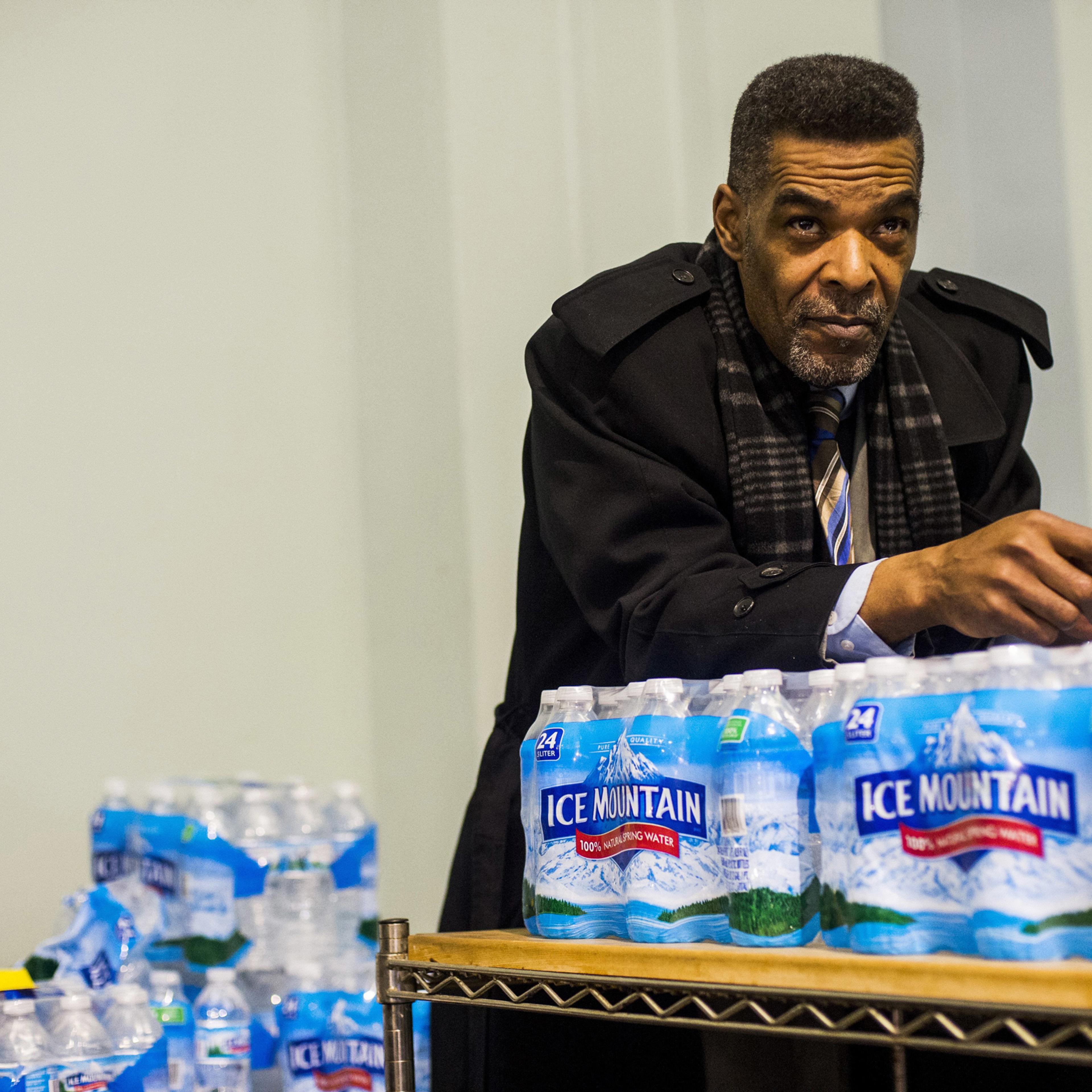 Flint City Councilman Eric Mays leans on a palette of water as he listens to health officials answer residents' questions during a Flint water town hall meeting at the University of Michigan-Flint Northbank Center in Flint, Mich. Flint officials, along w