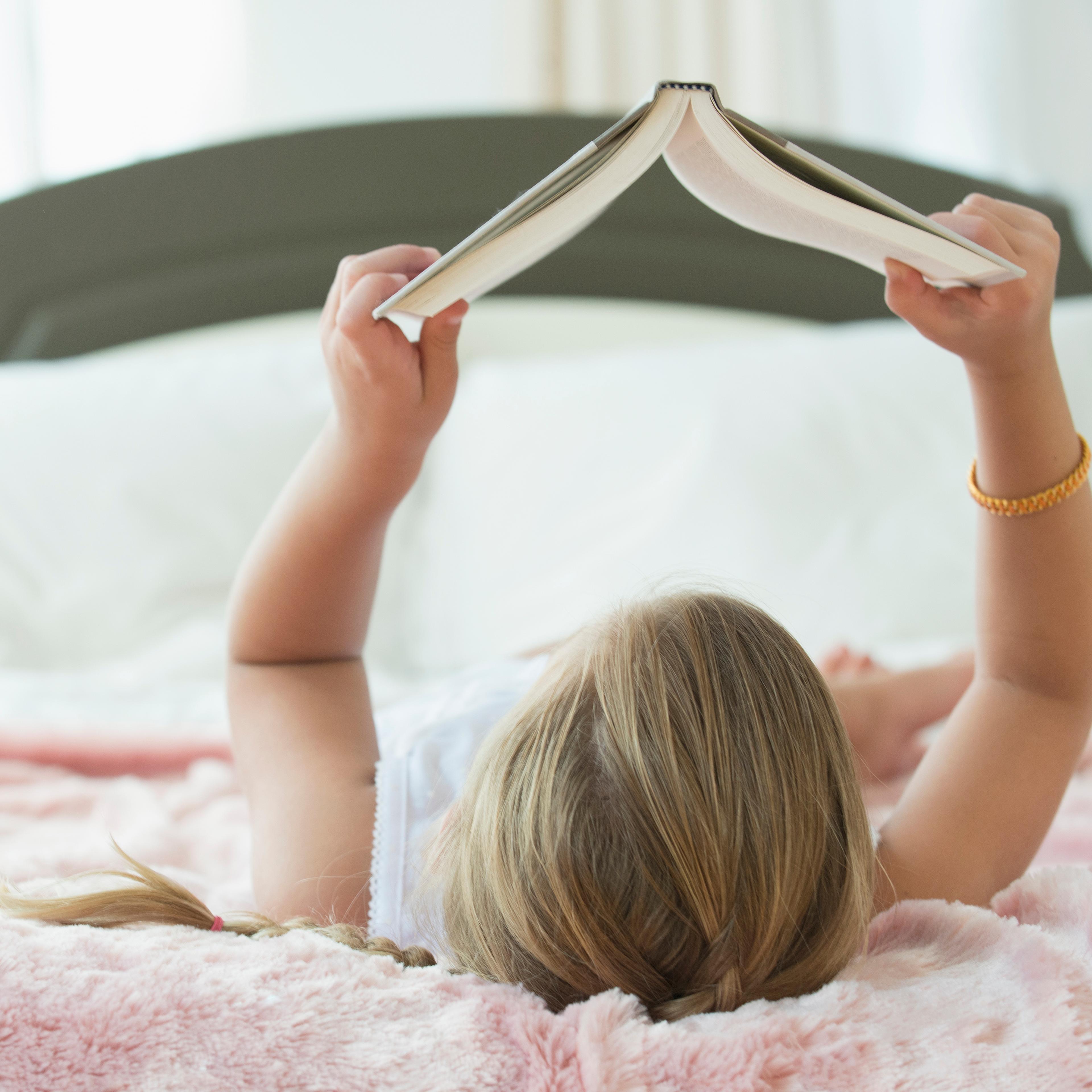 Caucasian girl laying on bed reading book
