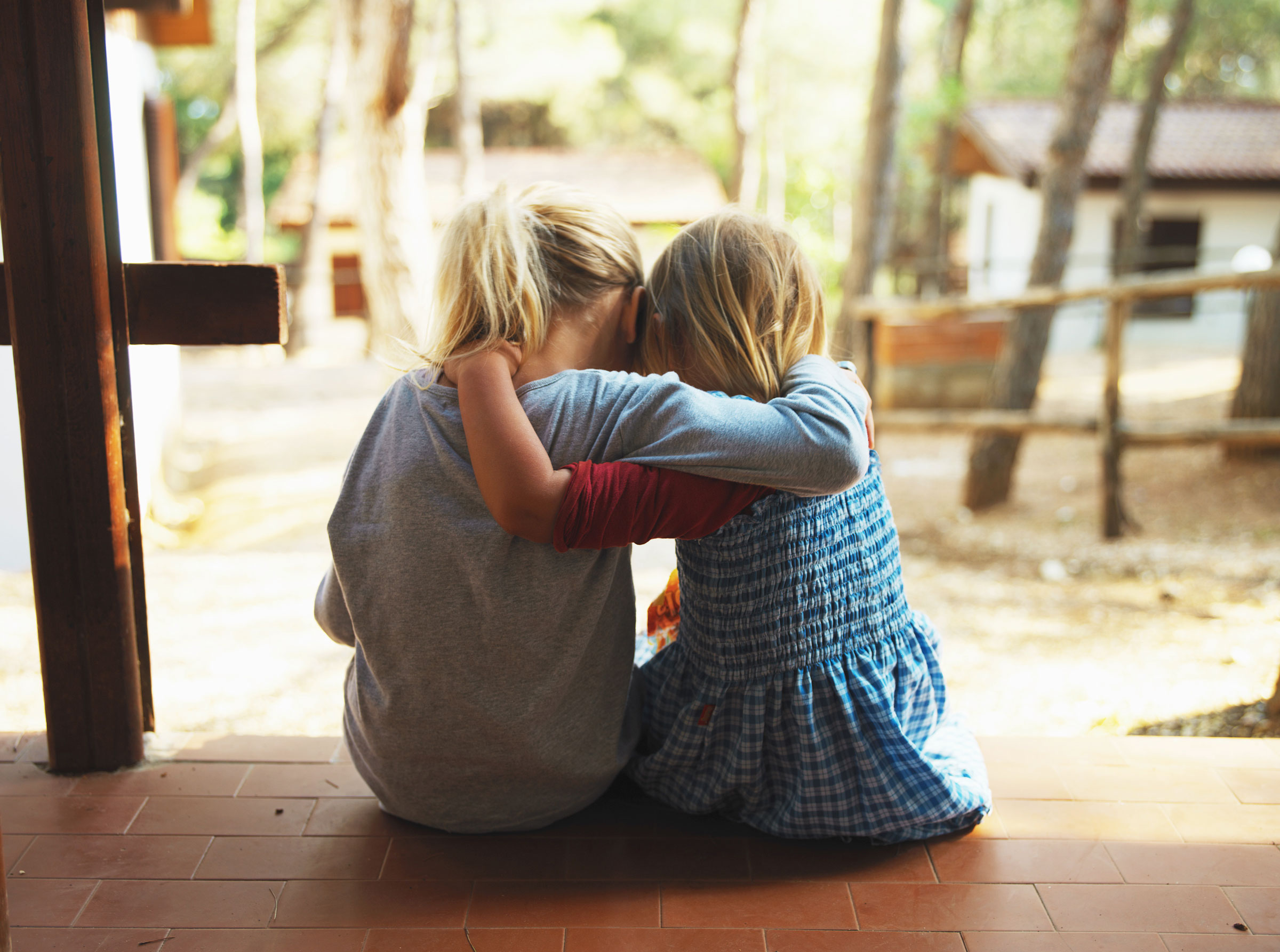 Two girls embracing on porch, rear view