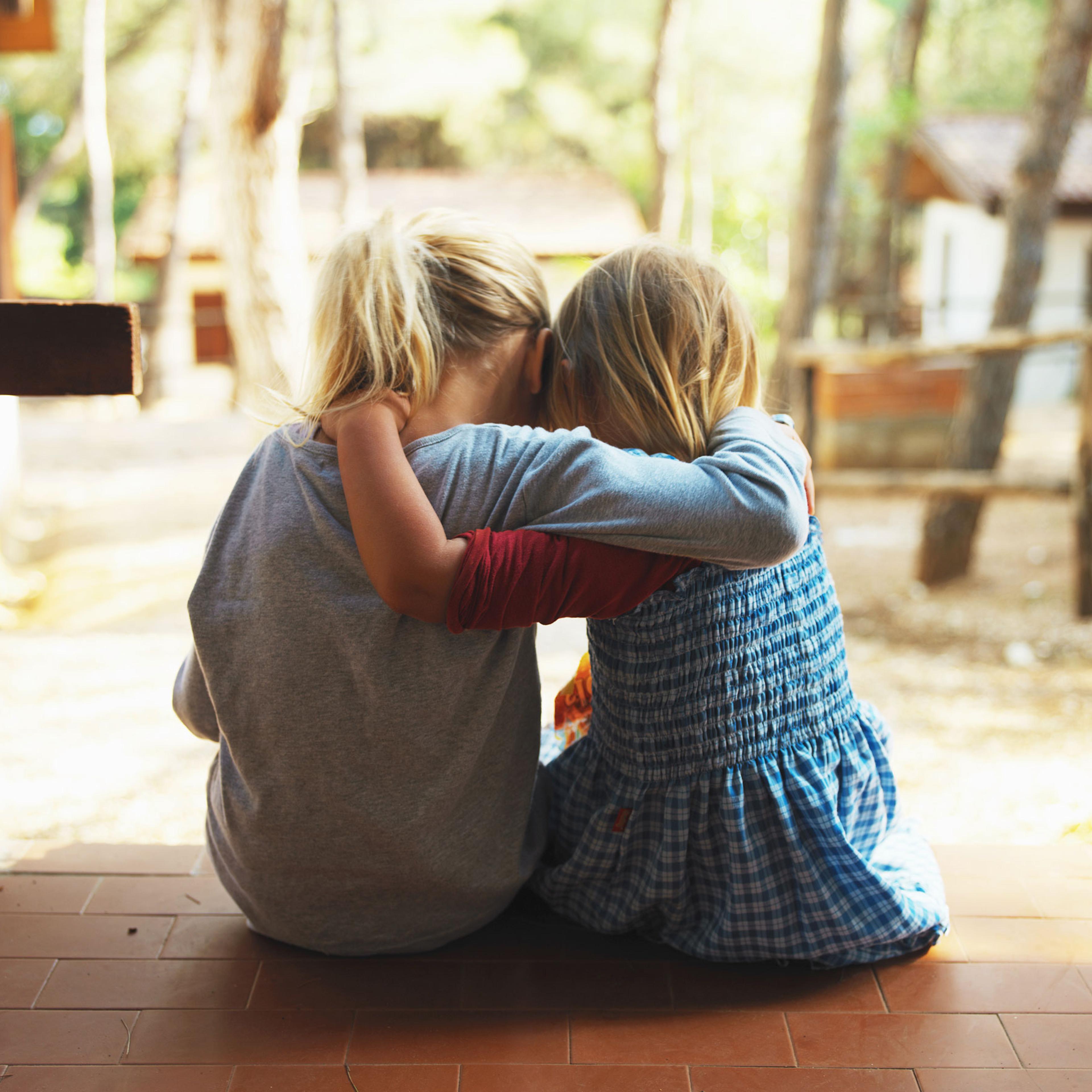 Two girls embracing on porch, rear view