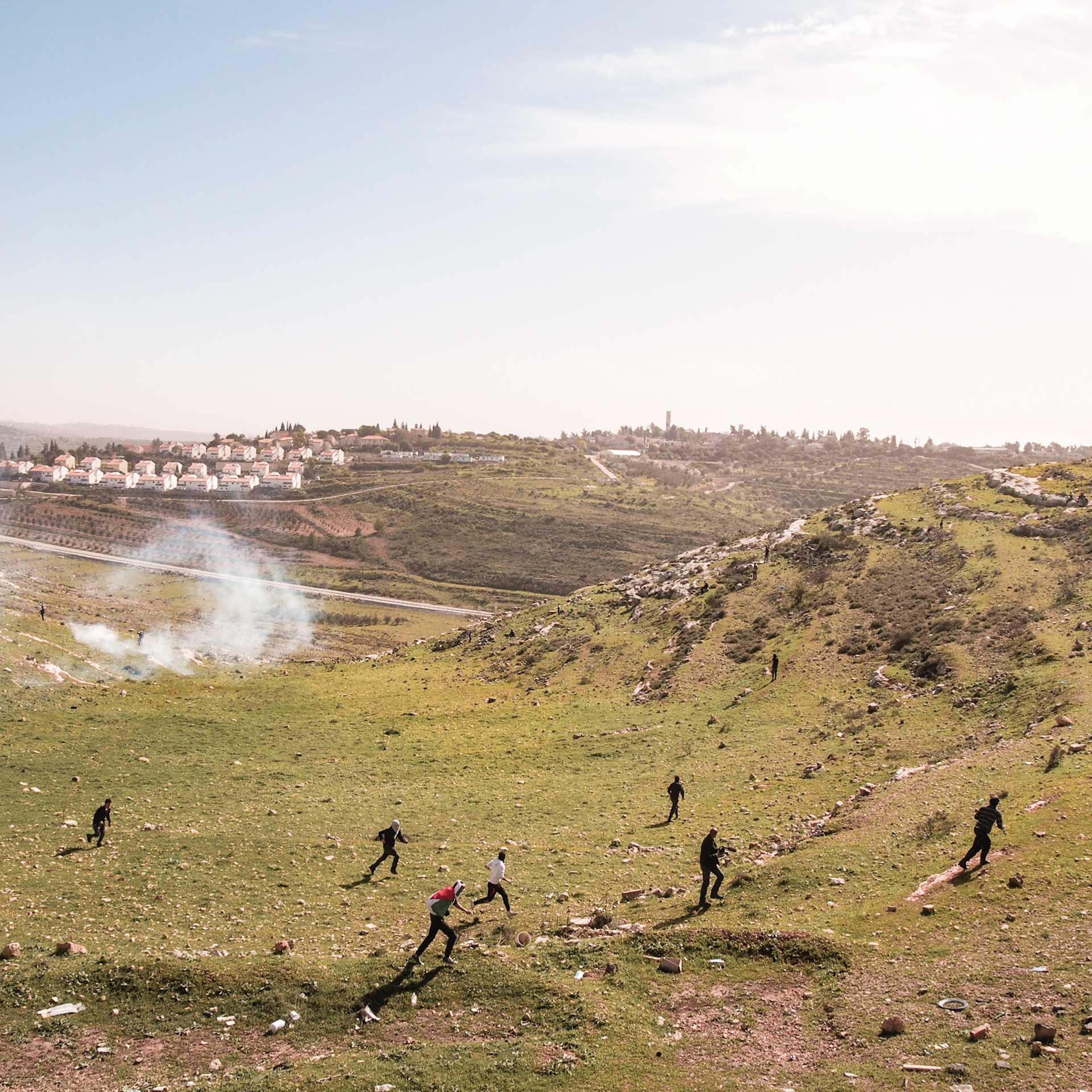West Bank, Nabi Saleh. 2013. Protestors run away as Israeli soldiers fire tear gas at them. The Israeli settlement of Halimish is in the background.Residents of Nabi Saleh have been protesting the Israeli Occupation every Friday after midday prayers sinc