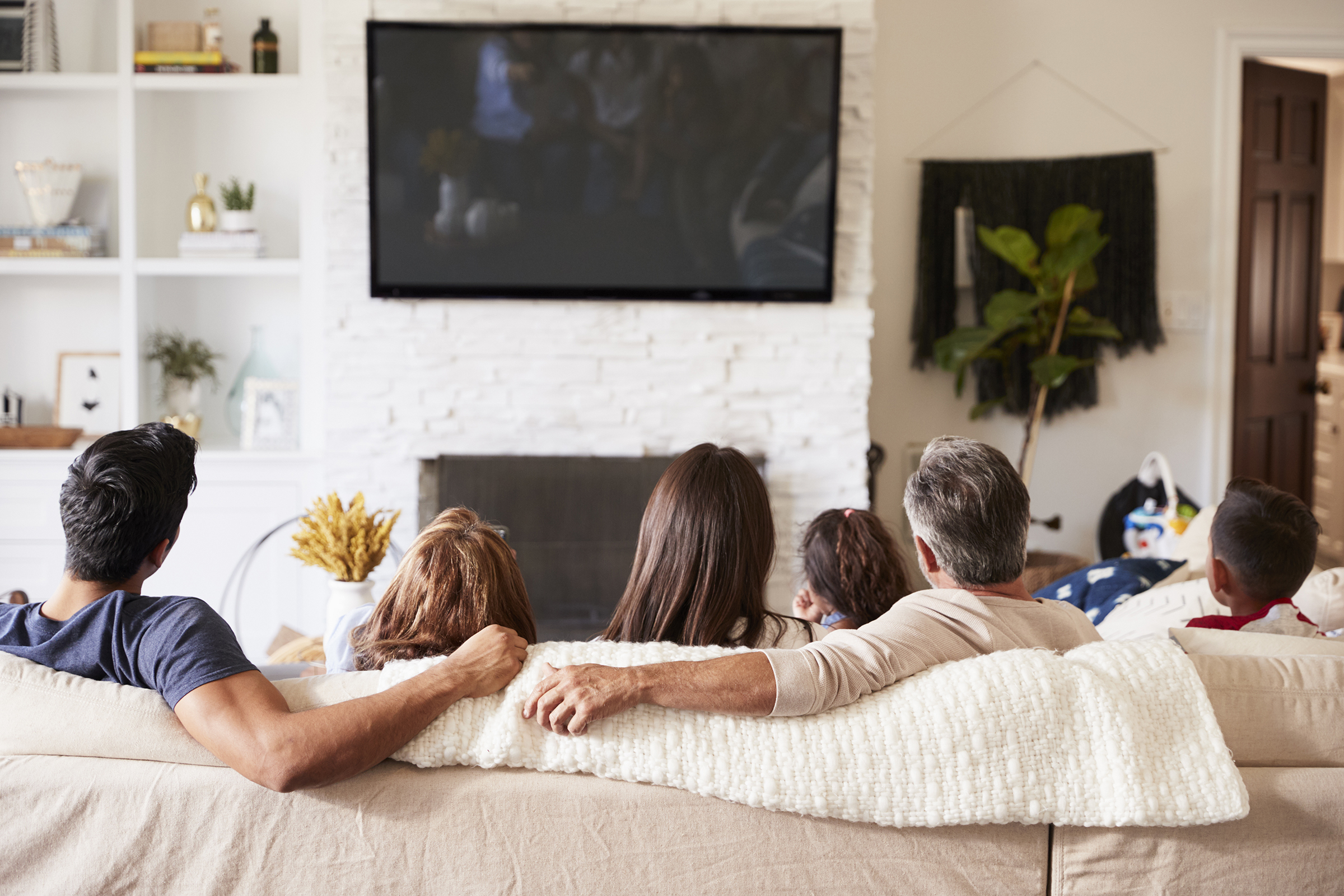 Back view of three generation Hispanic family sitting on the sofa watching TV