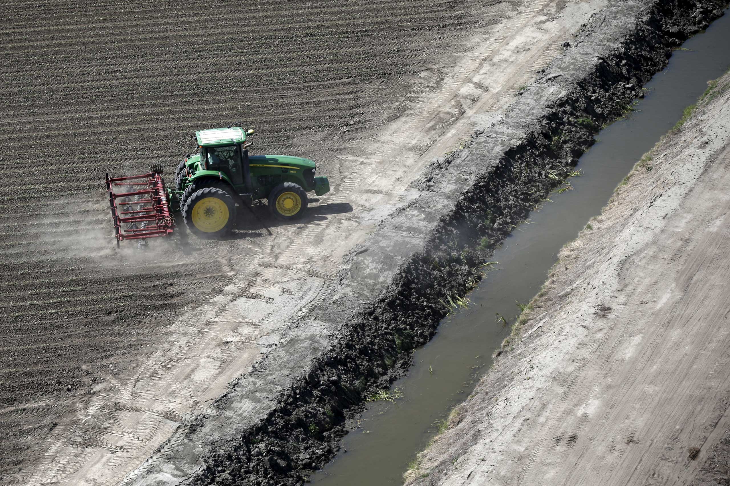A tractor ploughs a field next to a canal in Los Banos
