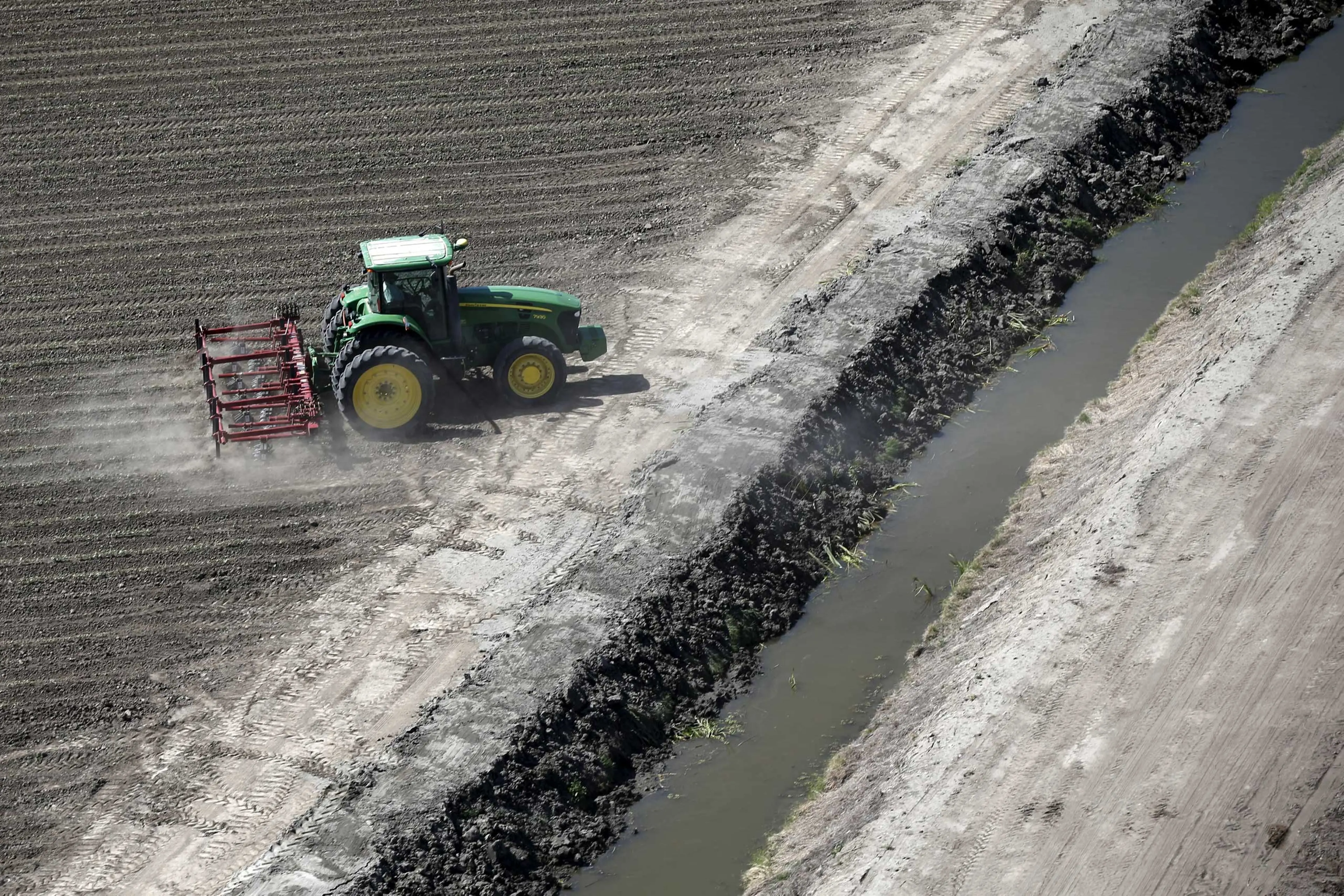 A tractor ploughs a field next to a canal in Los Banos