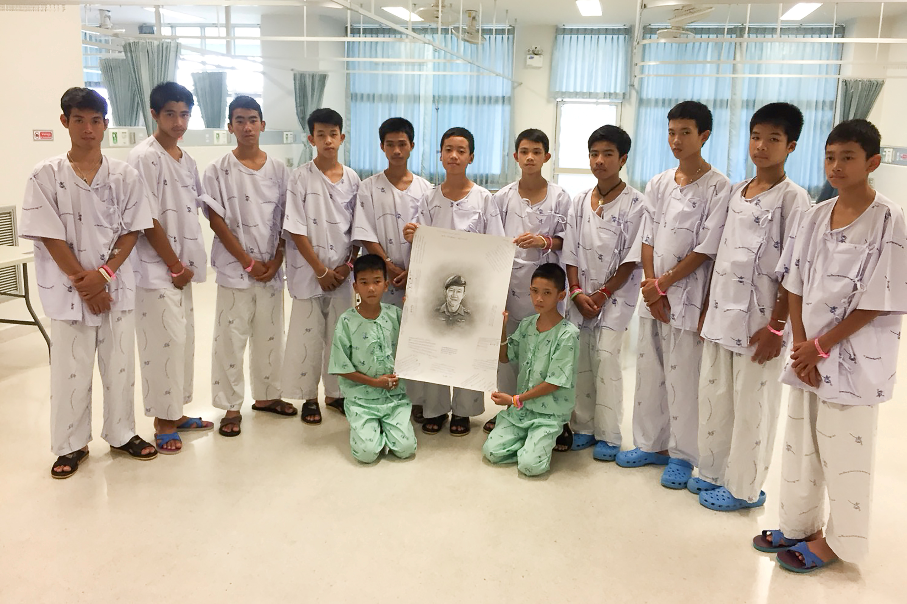 The 12-member "Wild Boars" soccer team and their coach rescued from a flooded cave pose with a drawing picture of Samarn Kunan, a former Thai navy diver who died working to rescue them at the Chiang Rai Prachanukroh Hospital, in Chiang Rai