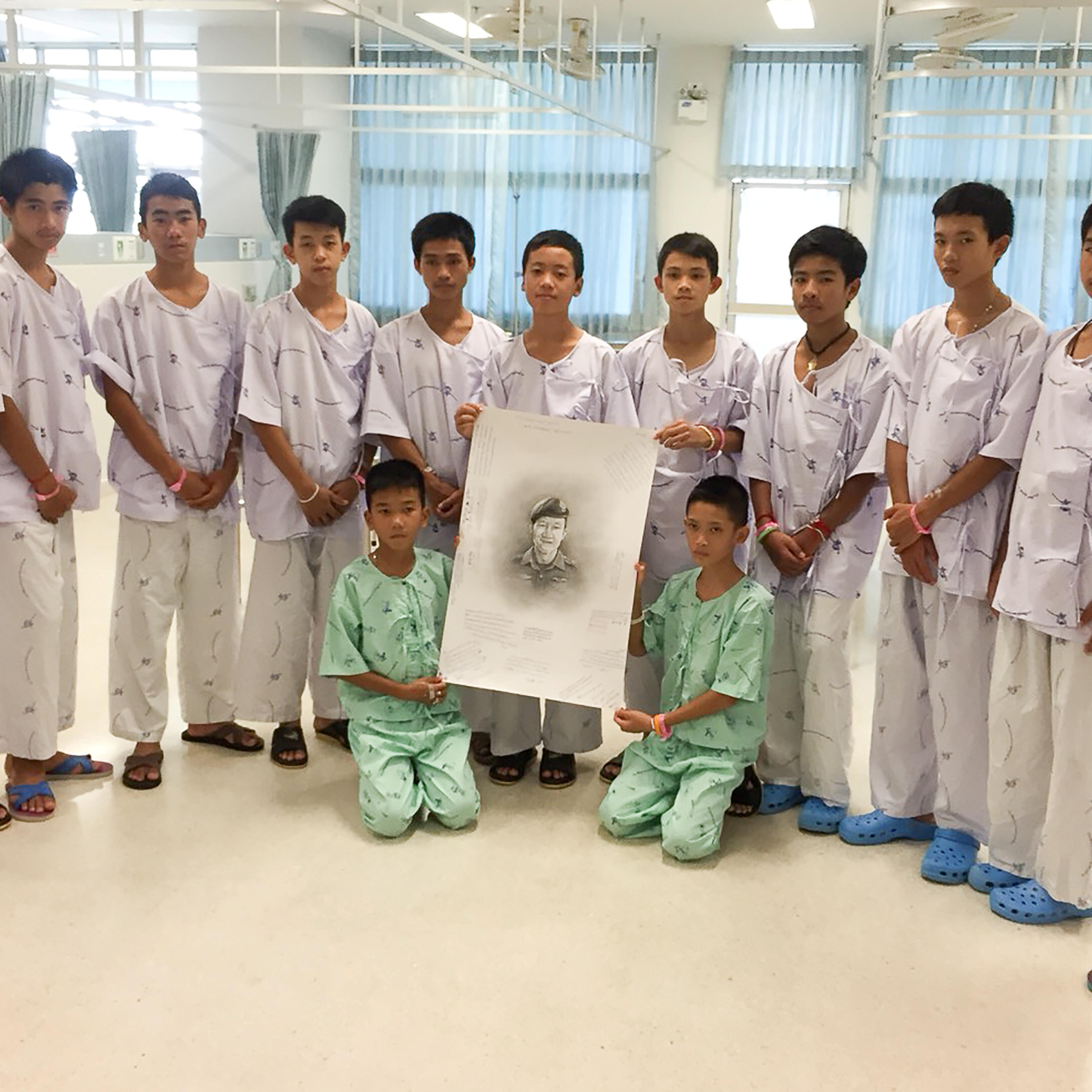 The 12-member "Wild Boars" soccer team and their coach rescued from a flooded cave pose with a drawing picture of Samarn Kunan, a former Thai navy diver who died working to rescue them at the Chiang Rai Prachanukroh Hospital, in Chiang Rai