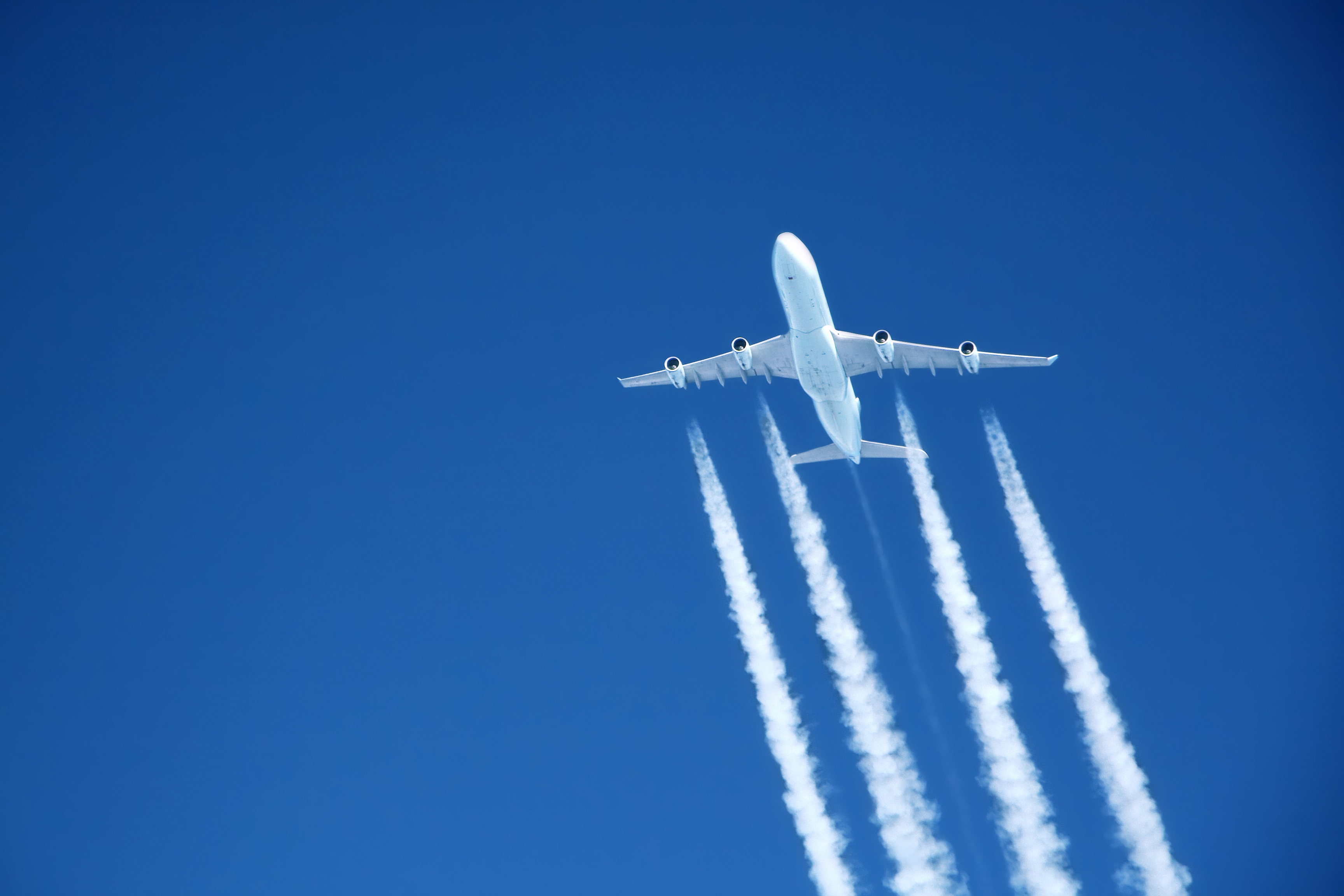 contrails streaming from a jumbo jet on blue sky at altitude