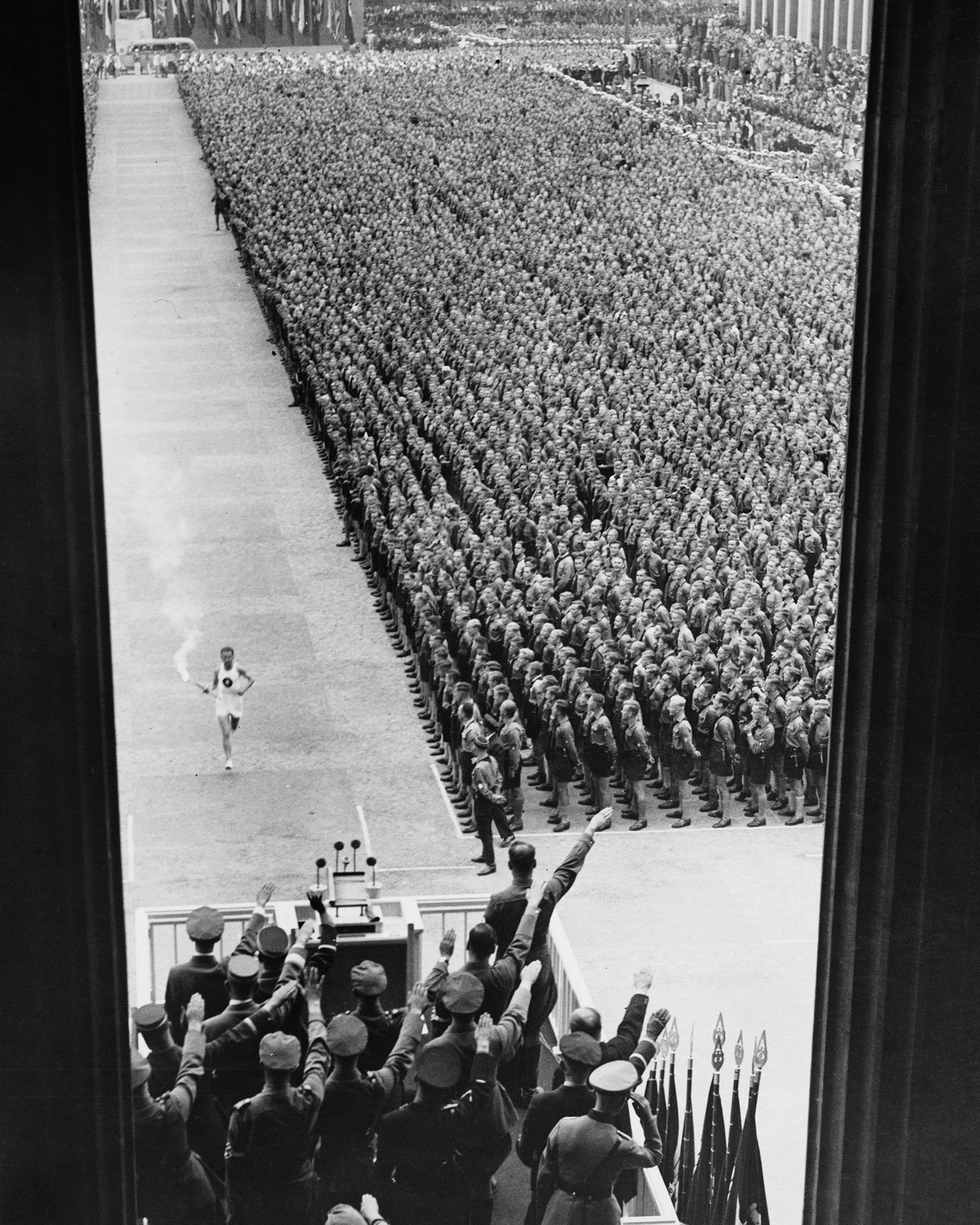 German athlete Fritz Schilgen runs past German army soldiers with the Olympic torch on his way to lighting the Olympic flame at the opening ceremony of the 1936 Summer Olympics at the Olympiastadion in Berlin, Germany, on Aug. 1 1936.