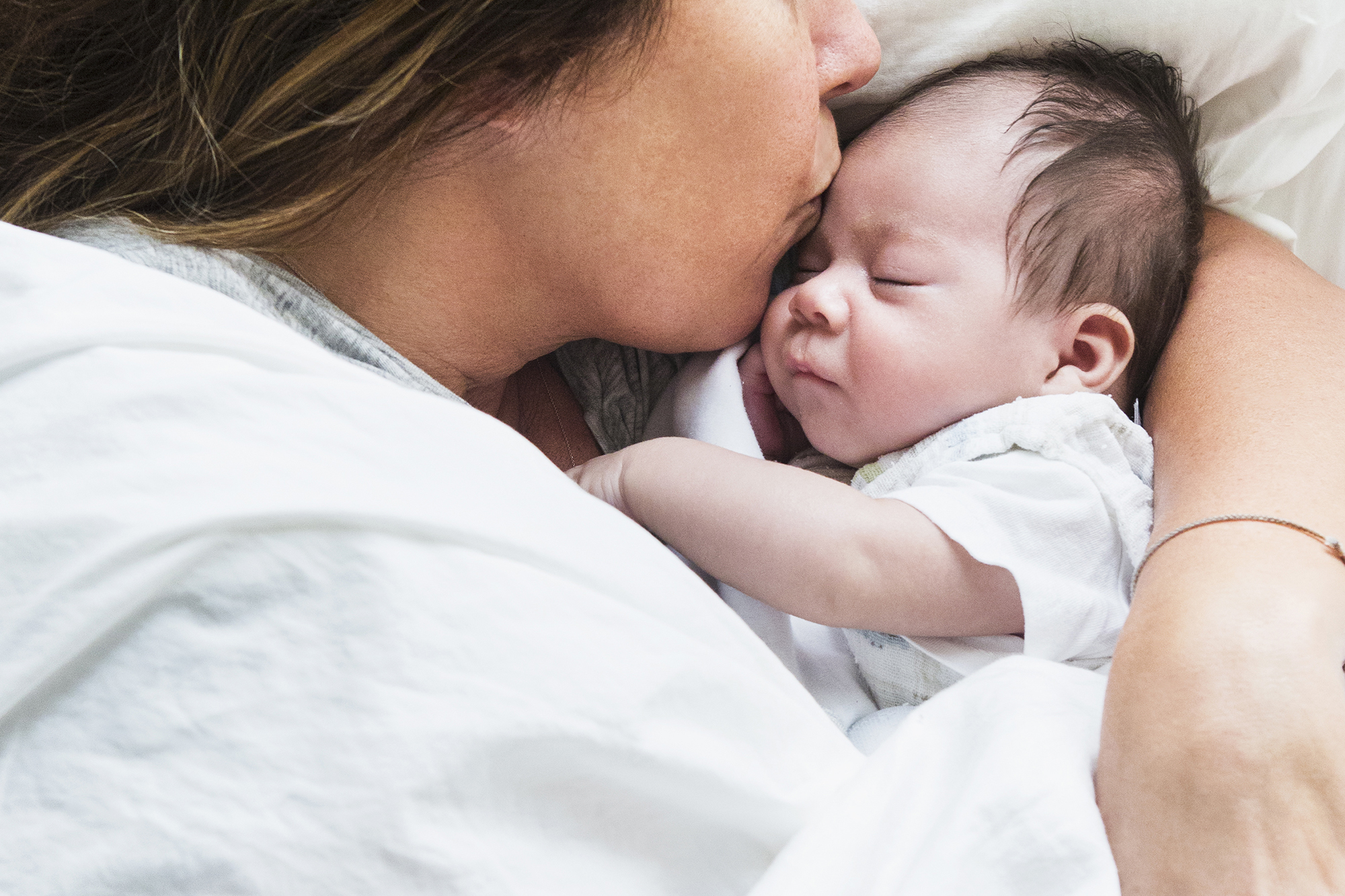 High angle view of mother kissing baby in bed