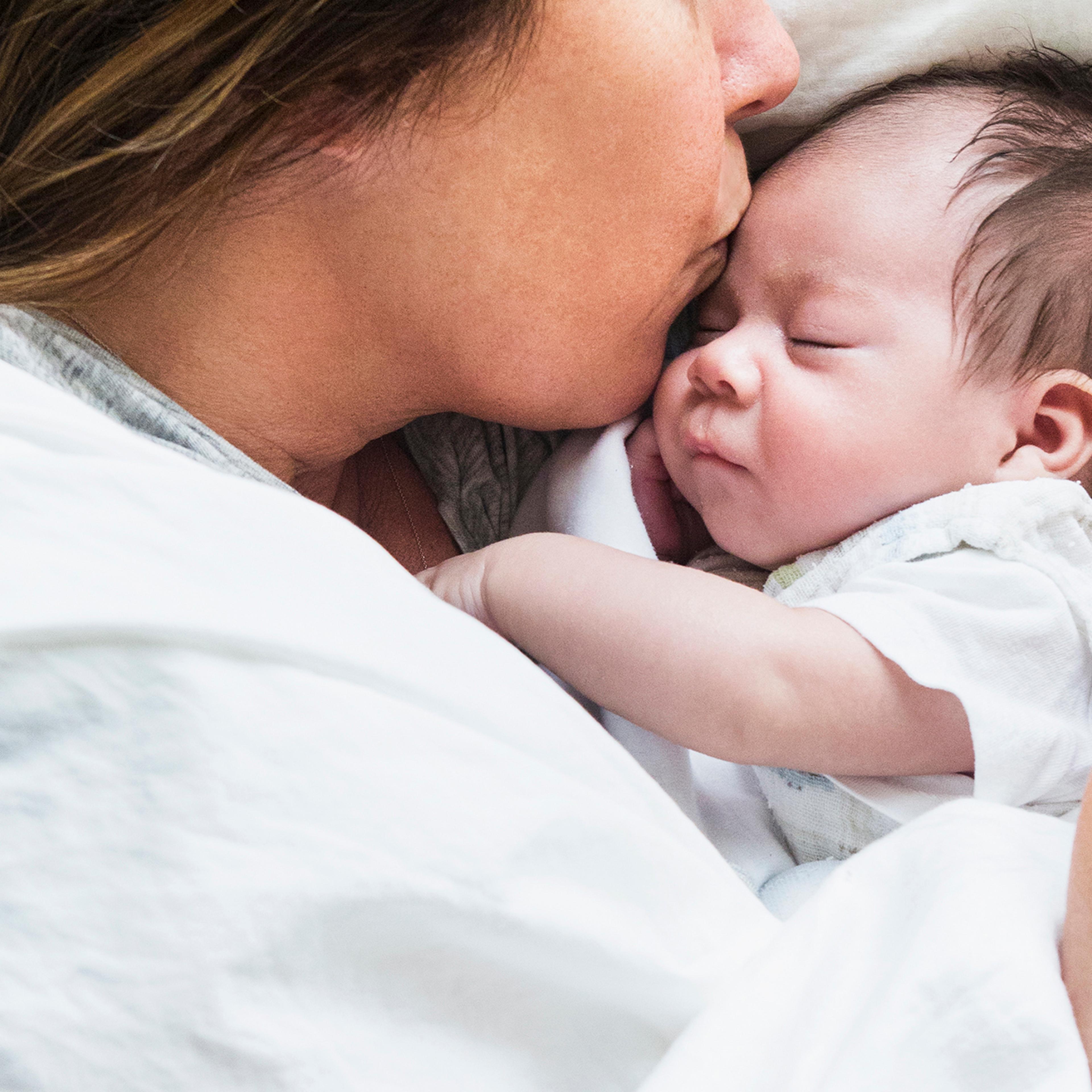 High angle view of mother kissing baby in bed
