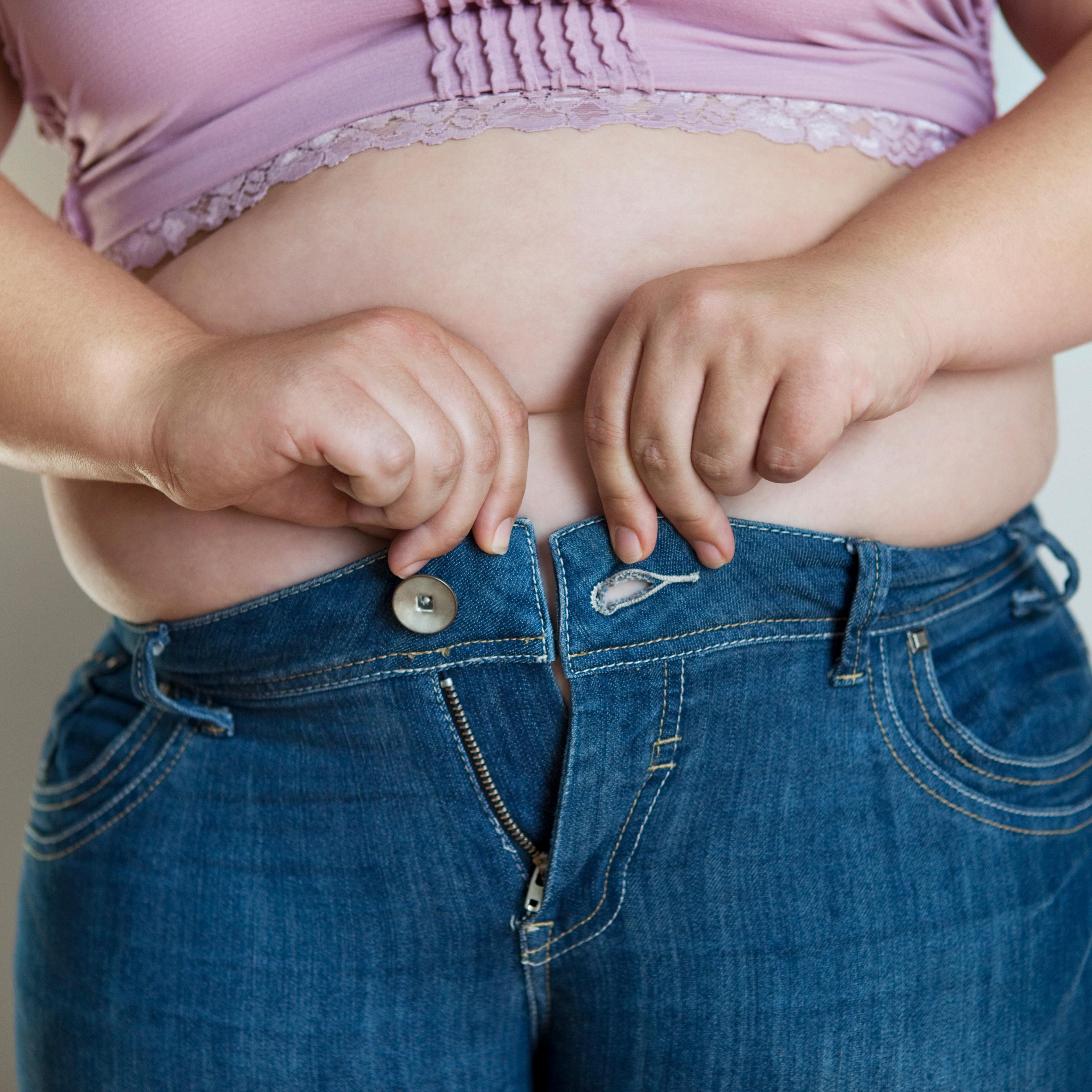 Overweight woman trying to fasten very tight jeans