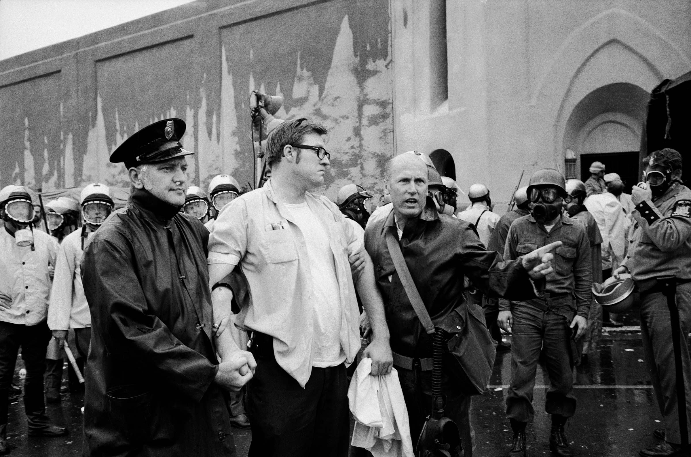 Prisoner being led away by guards while other officers in protective masks wait to storm the prison during the Attica riots in 1971.