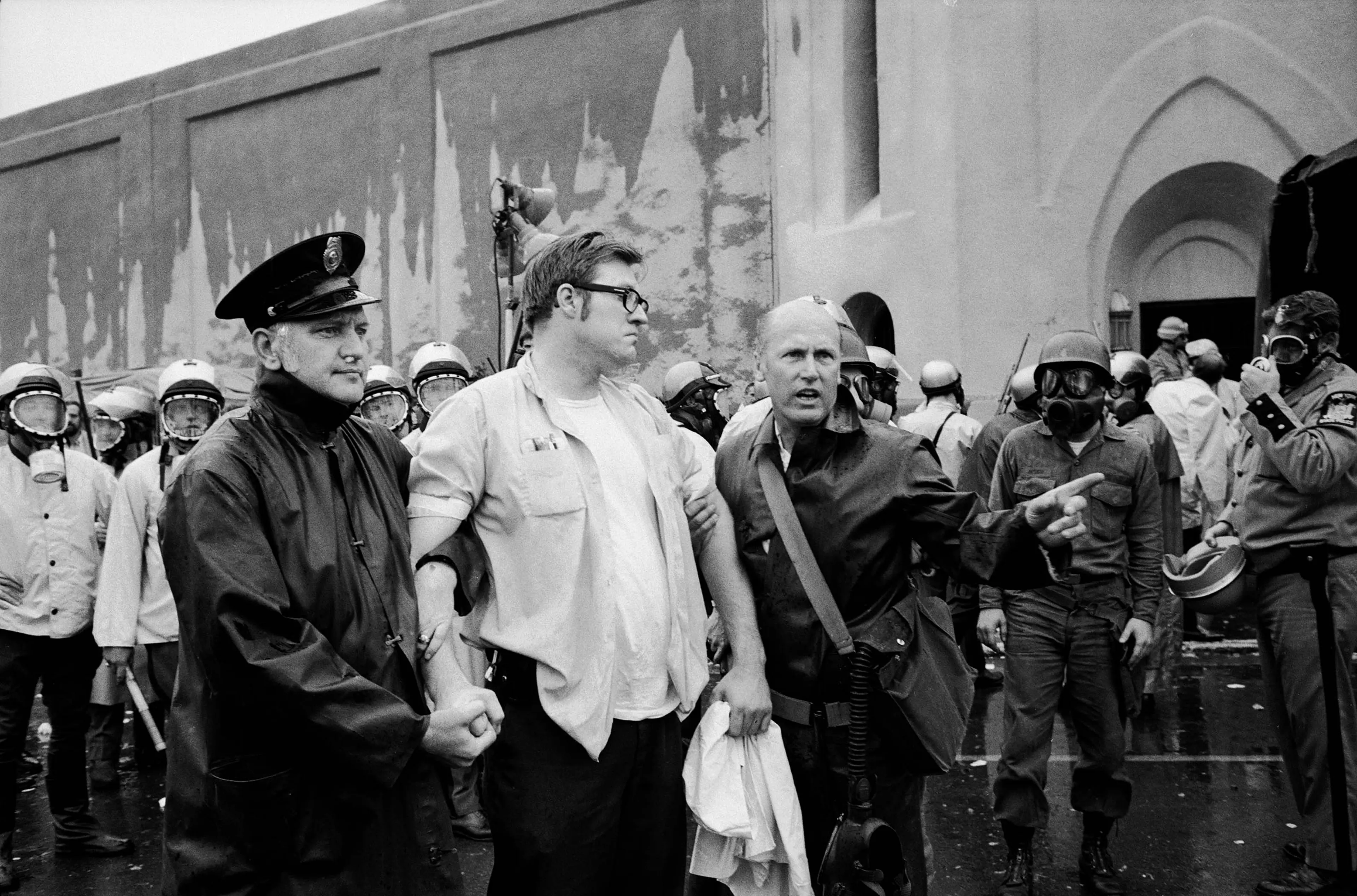 Prisoner being led away by guards while other officers in protective masks wait to storm the prison during the Attica riots in 1971.