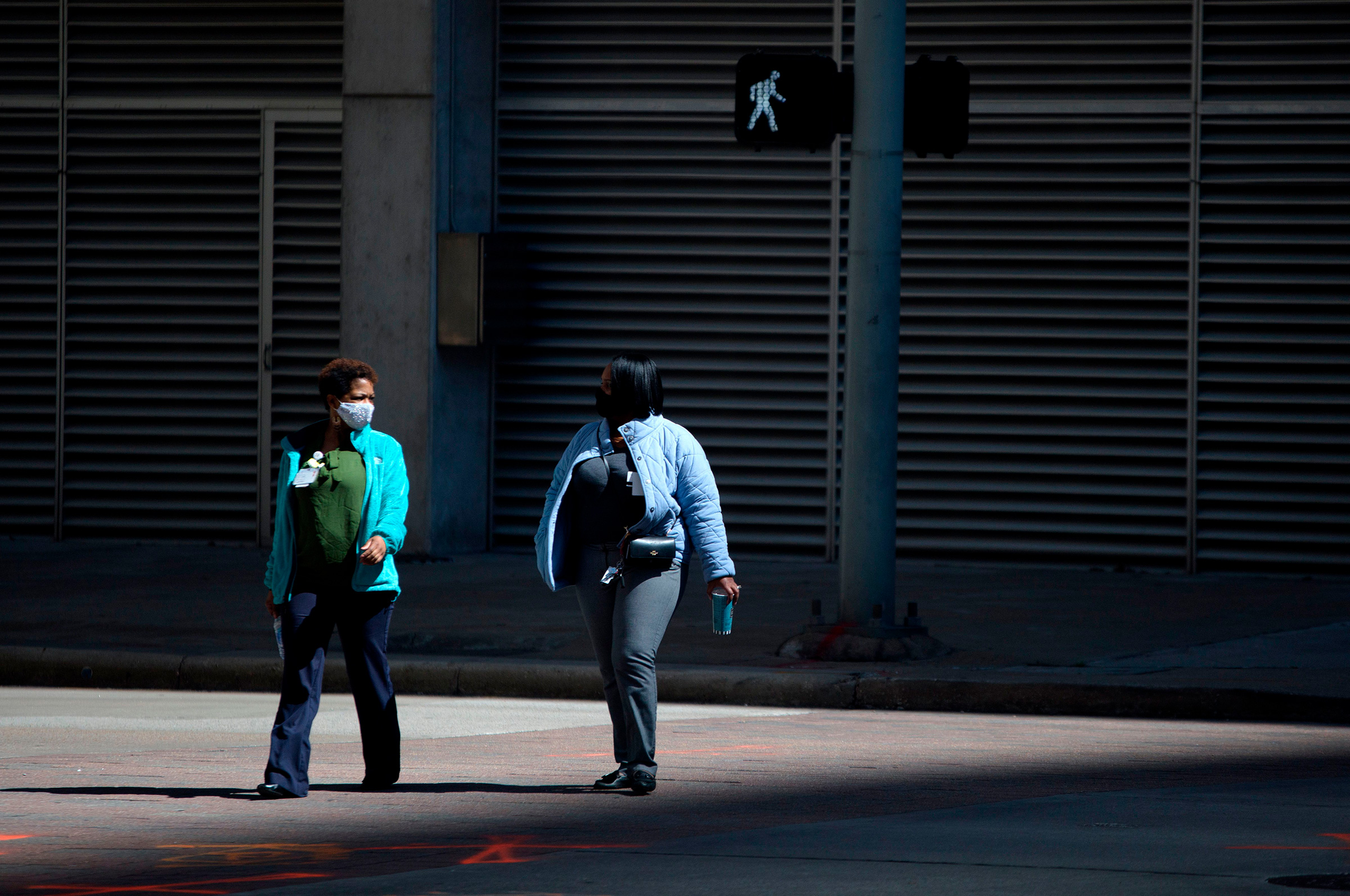 Pedestrians wear masks while walking across a street in downtown Houston, Texas on March 3, 2021.