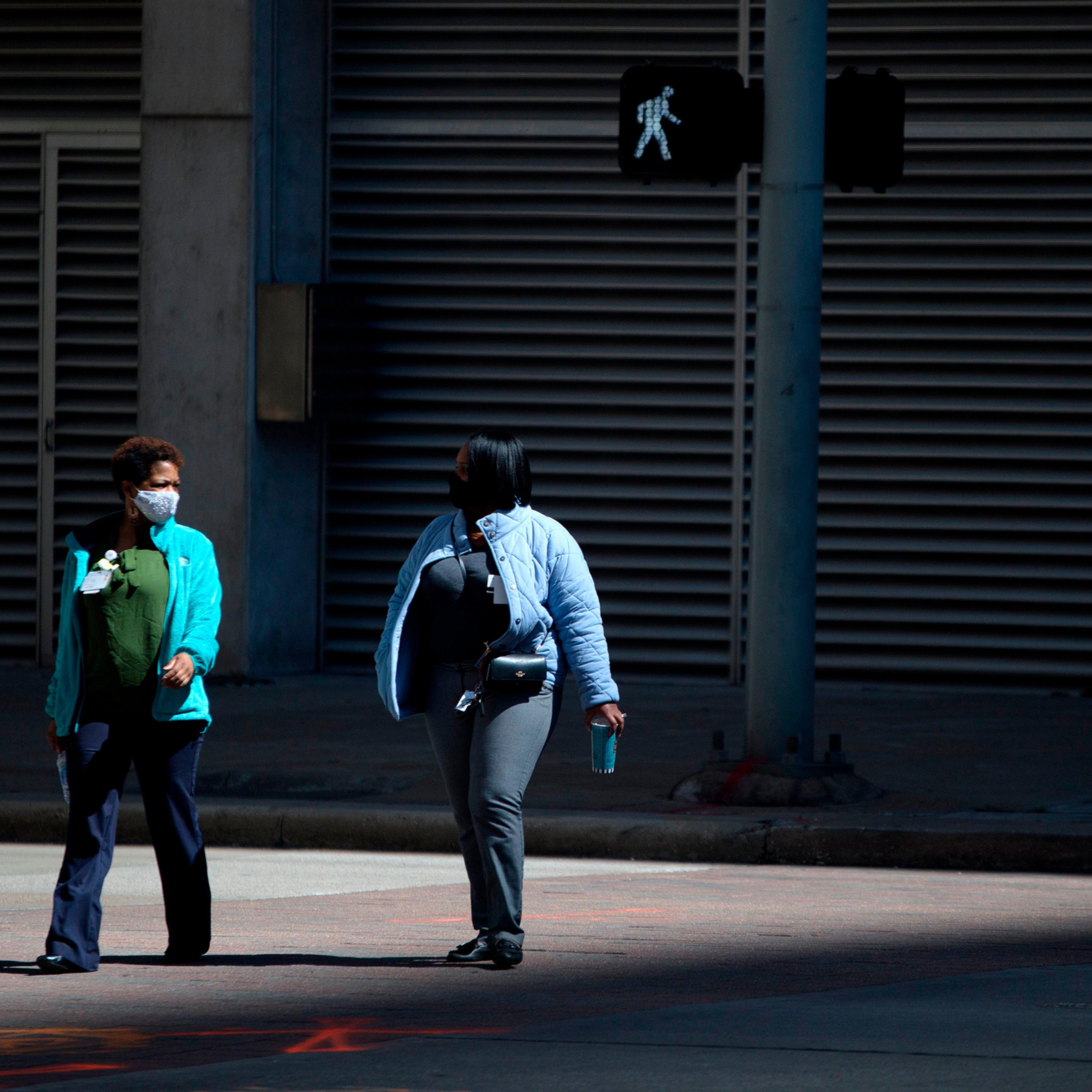 Pedestrians wear masks while walking across a street in downtown Houston, Texas on March 3, 2021.