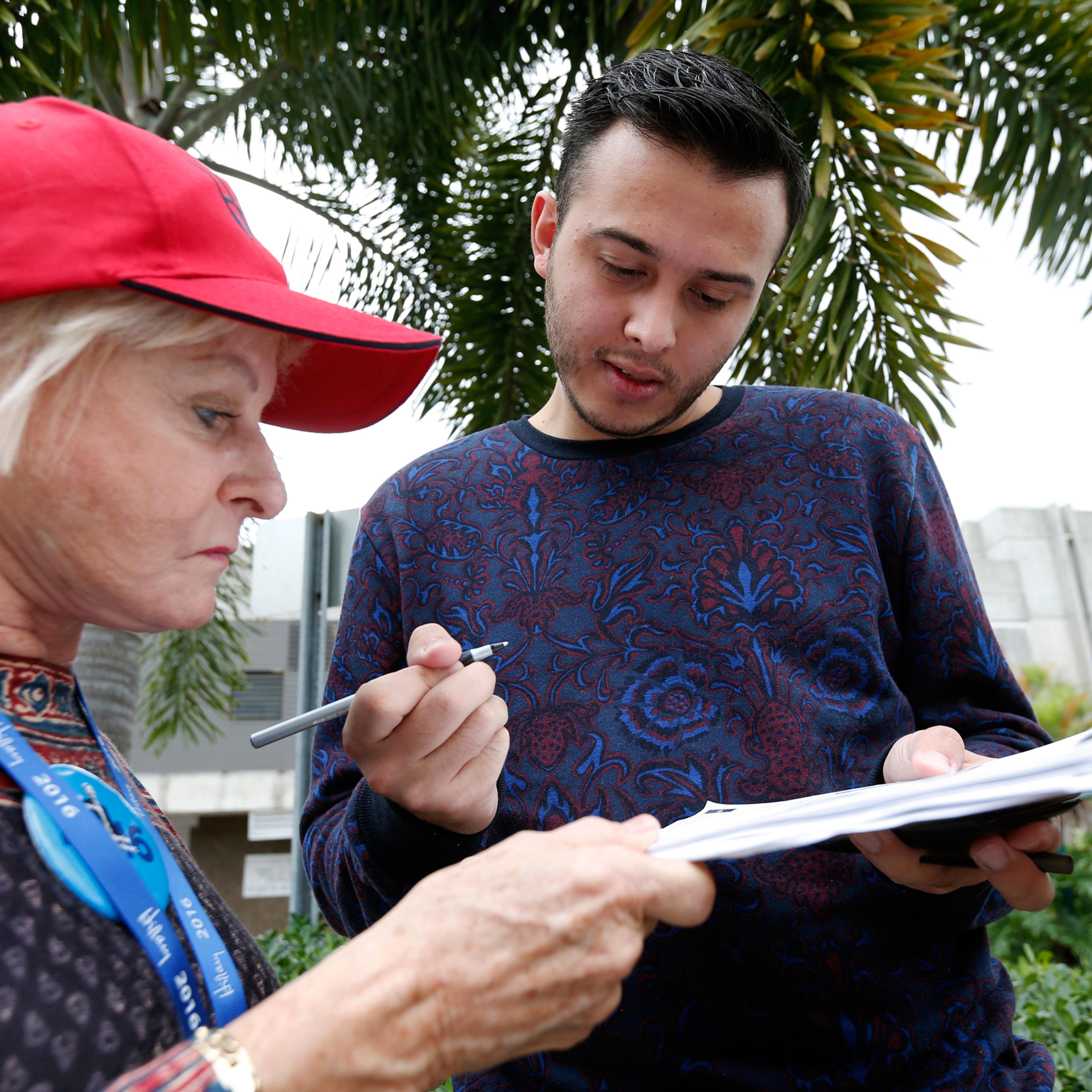 Volunteer Sandi Strickland, left, helps Roman Rodriguez, right, fill out a new voter registration form because of a change of address, as he waits in line to attend a rally for Democratic presidential candidate Hillary Clinton and former vice president A