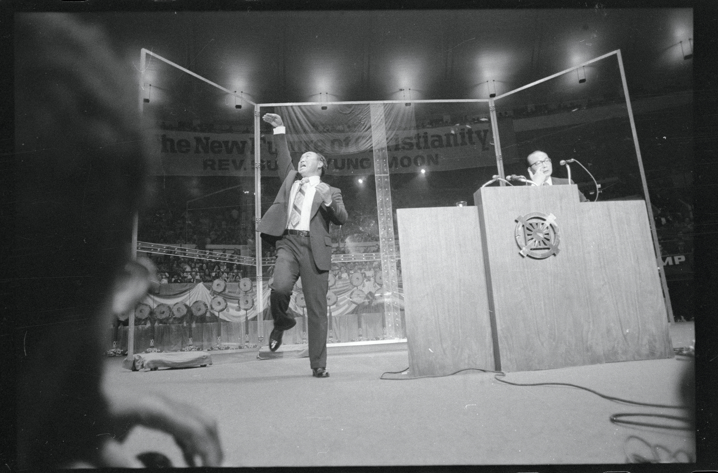 The Reverend Sun Myung Moon, Korean evangelist, gestures dramatically as he speaks at New York's Madison Square Garden. His chief associate, Col. Bo Hi Park, (right) translates the evangelist's Korean to English. The Reverend Moon said that God had told 