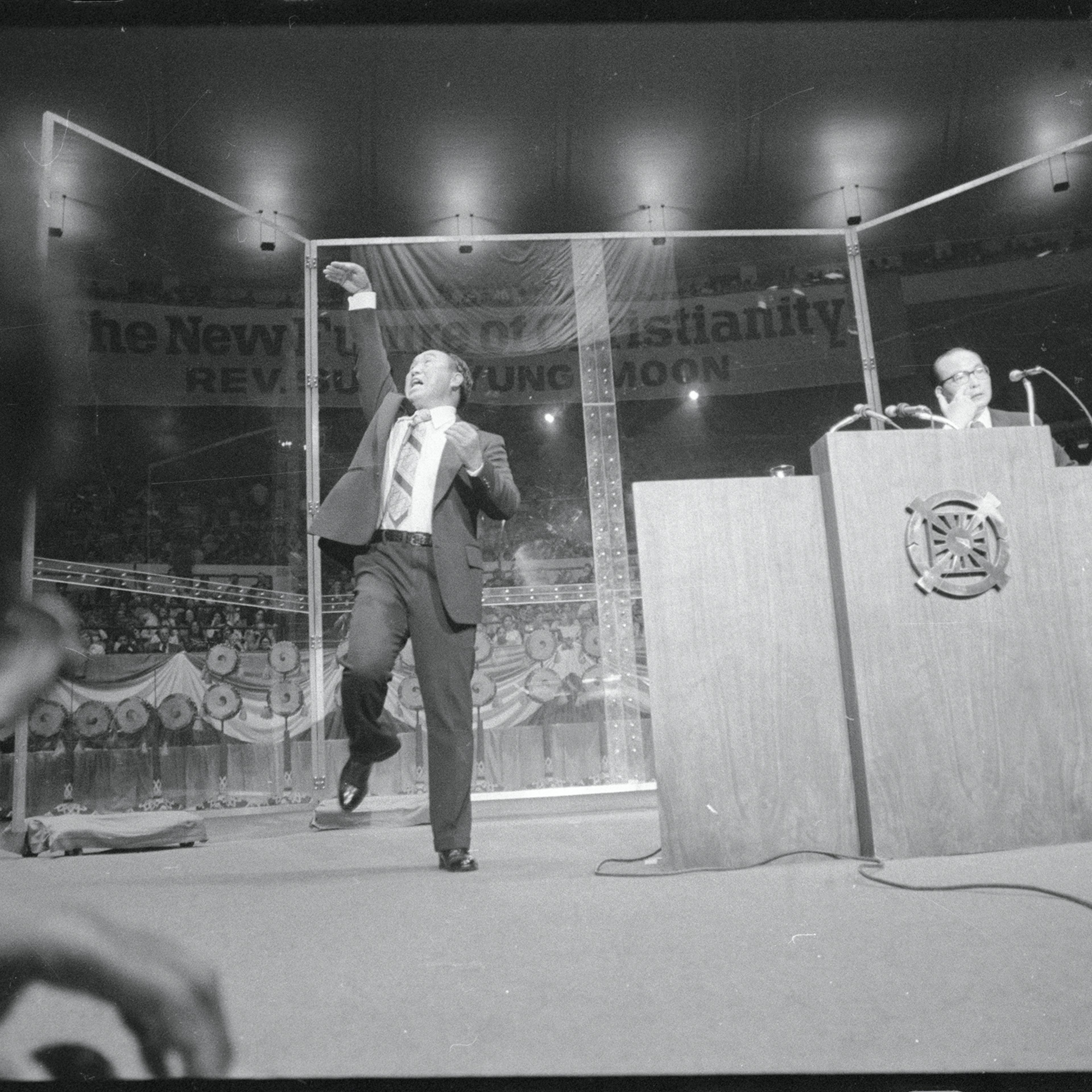 The Reverend Sun Myung Moon, Korean evangelist, gestures dramatically as he speaks at New York's Madison Square Garden. His chief associate, Col. Bo Hi Park, (right) translates the evangelist's Korean to English. The Reverend Moon said that God had told